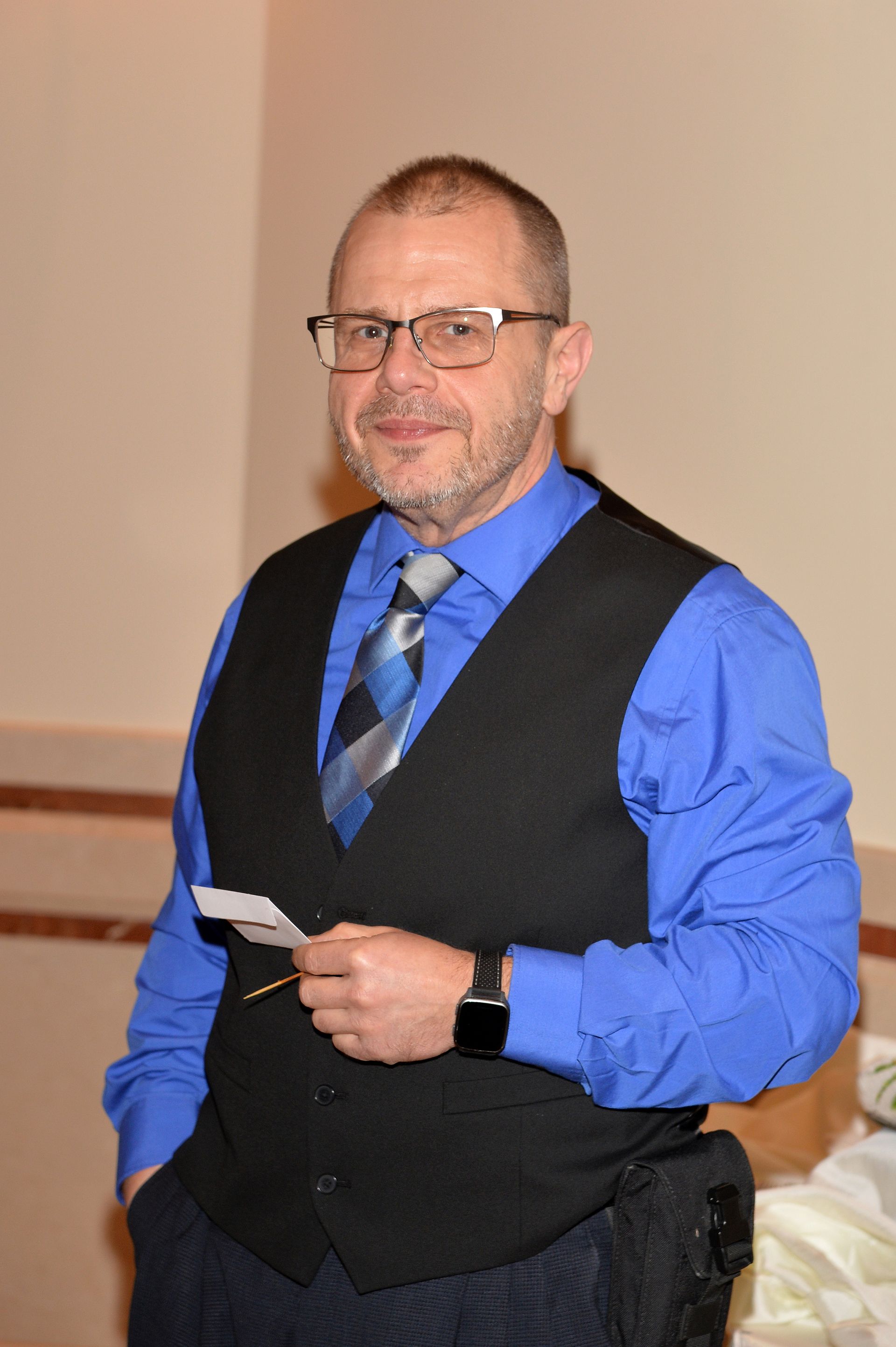A man in a blue shirt and black vest is holding a piece of paper.