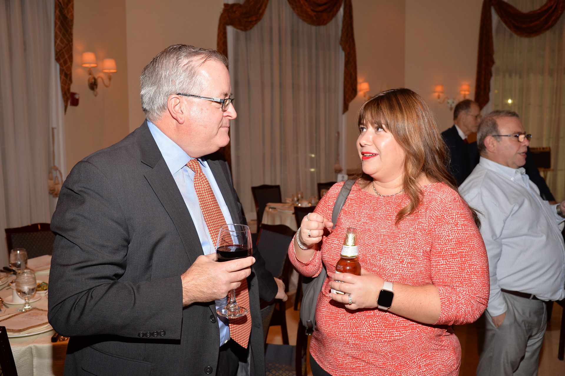 A man in a suit and tie is talking to a woman in a red sweater.