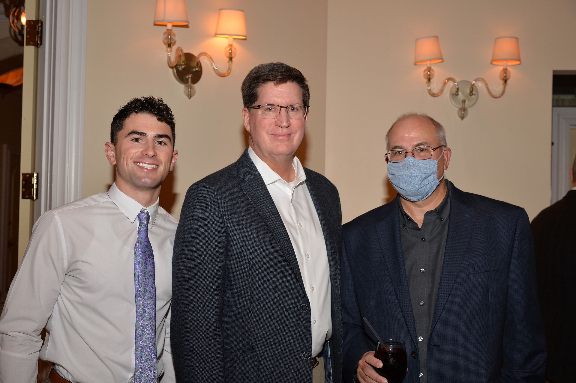 Three men are posing for a picture in a room . one of the men is wearing a mask.