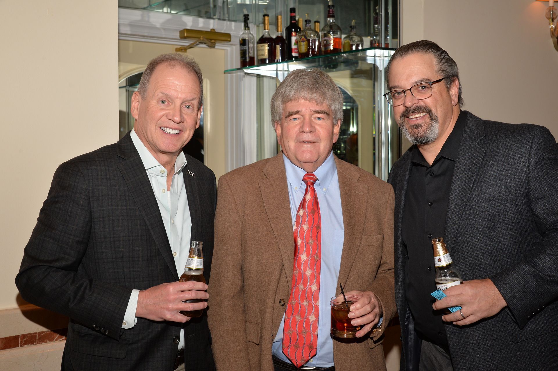 Three men are standing next to each other holding bottles of beer.