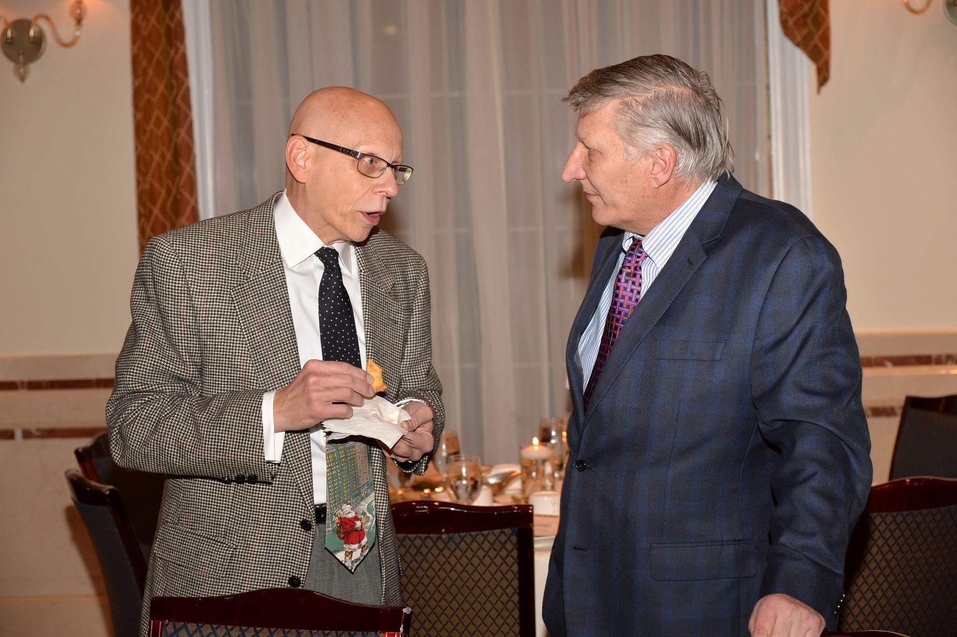 Two men in suits and ties are talking to each other in a room.