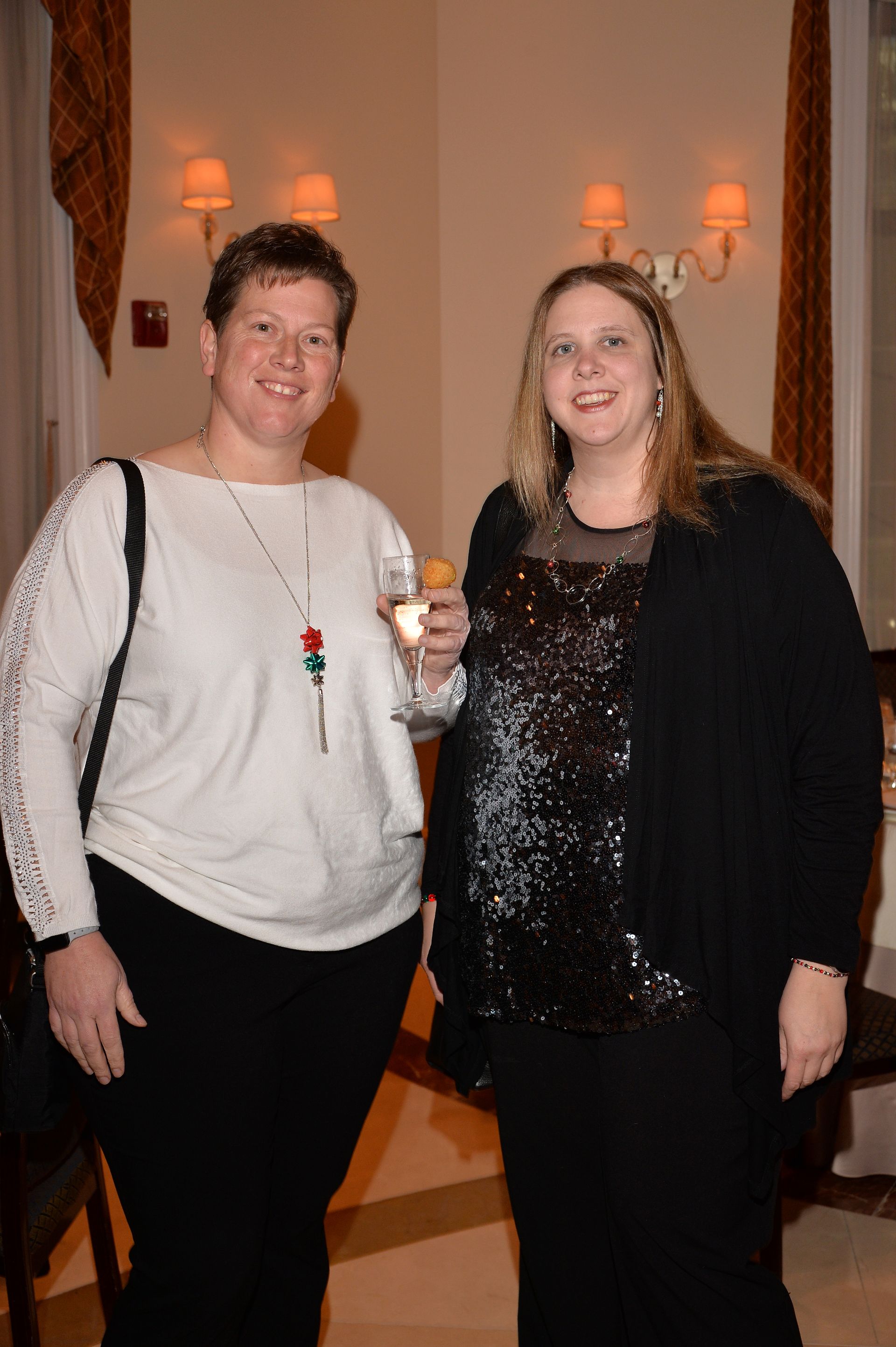 Two women are standing next to each other in a room holding glasses of wine.