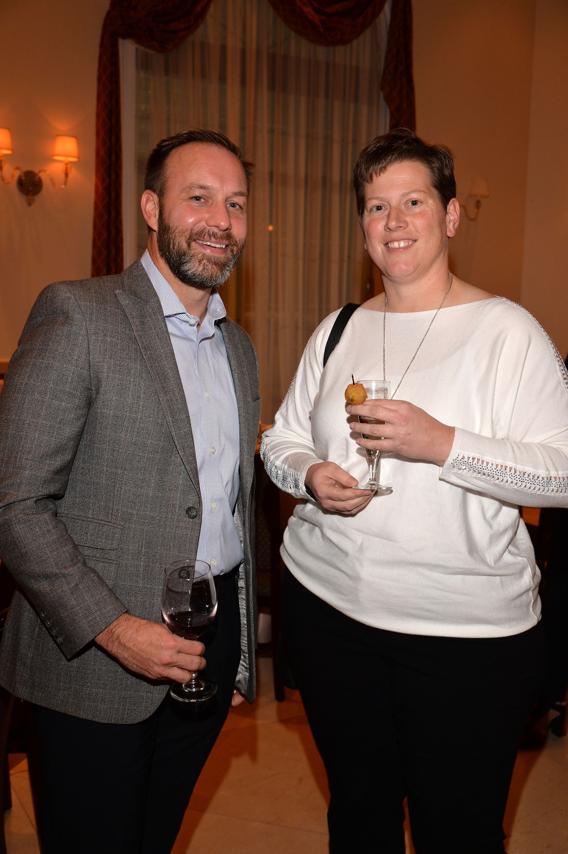 A man and a woman are standing next to each other holding wine glasses.
