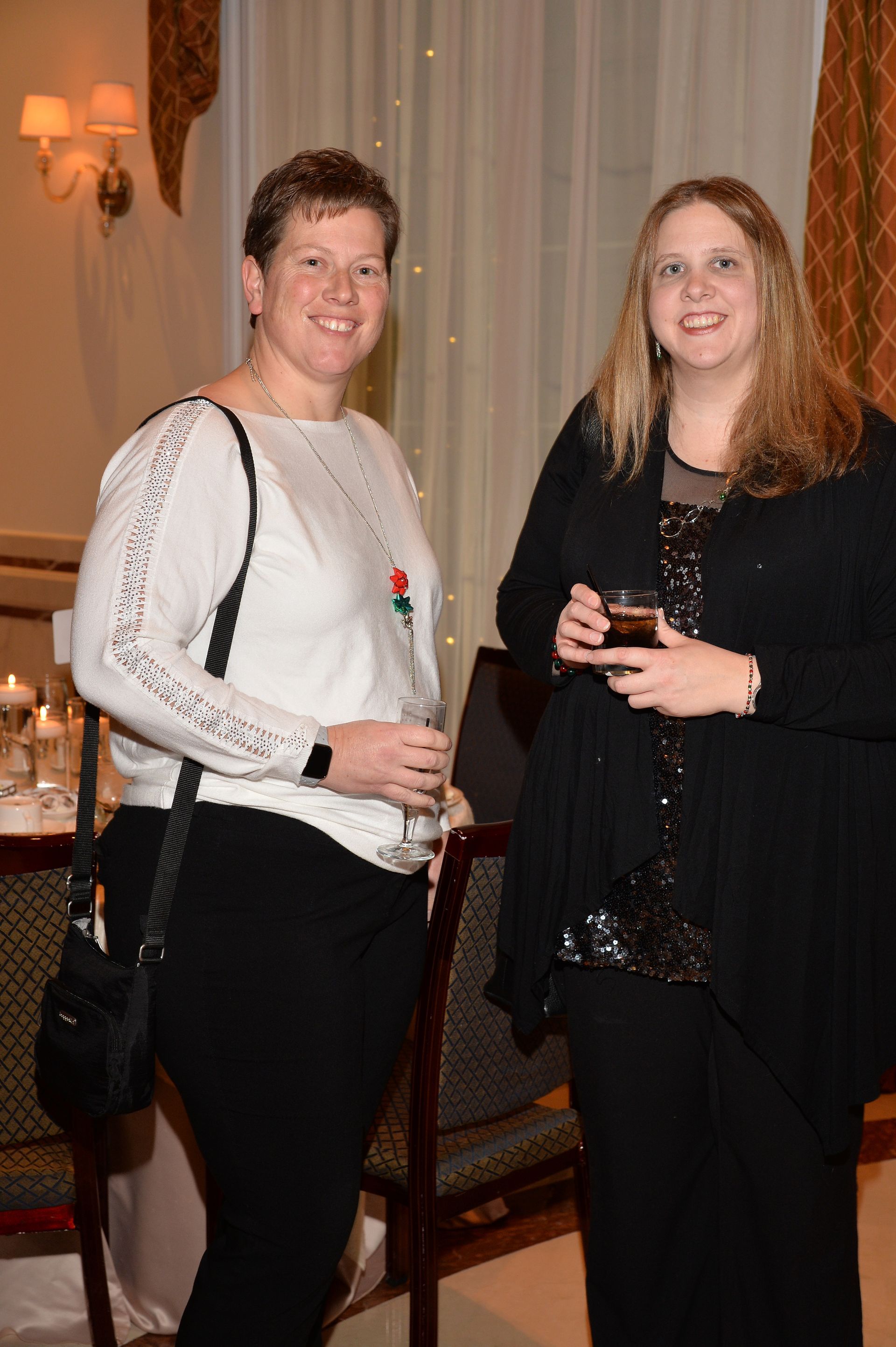 Two women are standing next to each other in a room holding wine glasses.