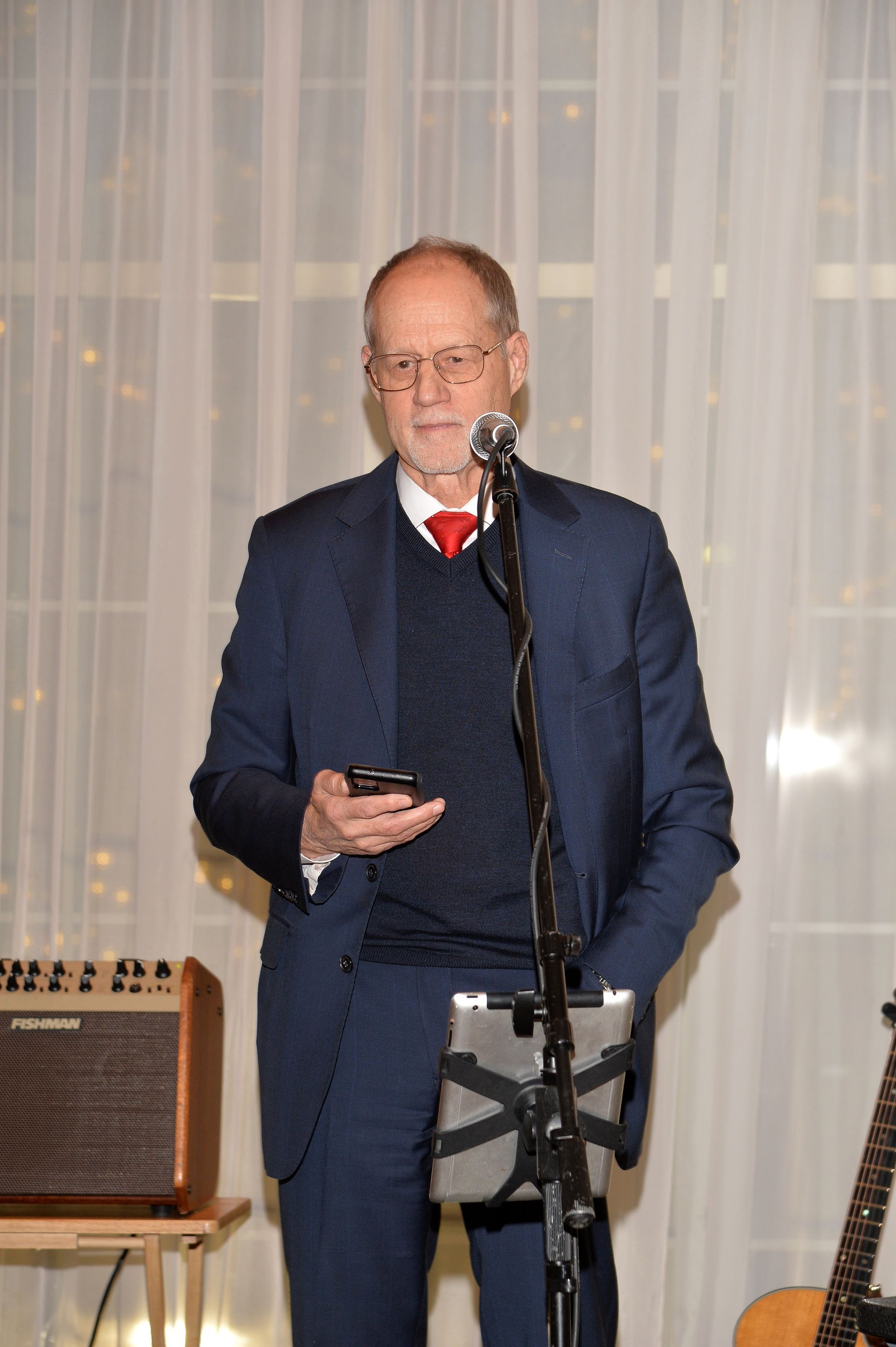 A man in a suit is singing into a microphone while holding a tablet.