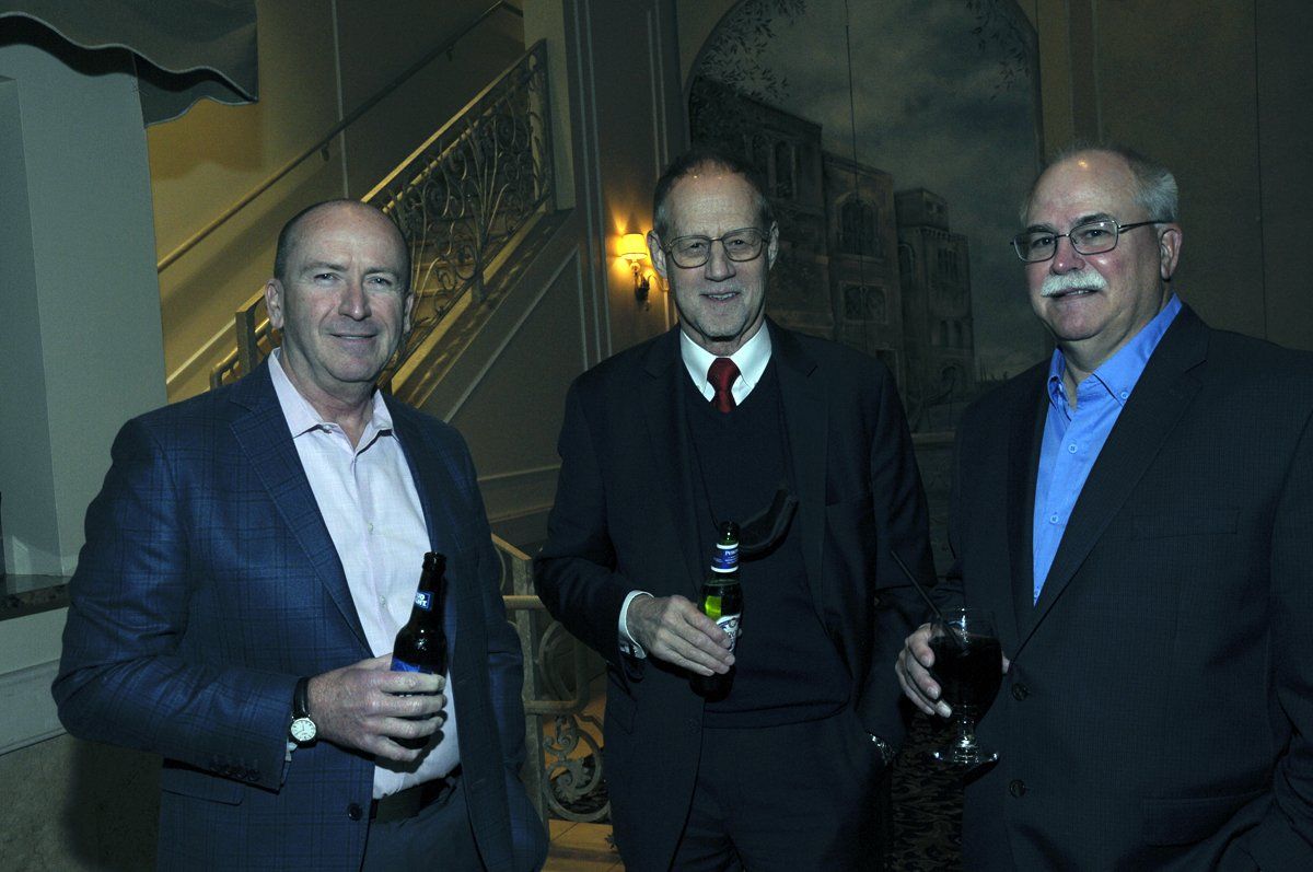 Three men are standing next to each other holding bottles of wine.