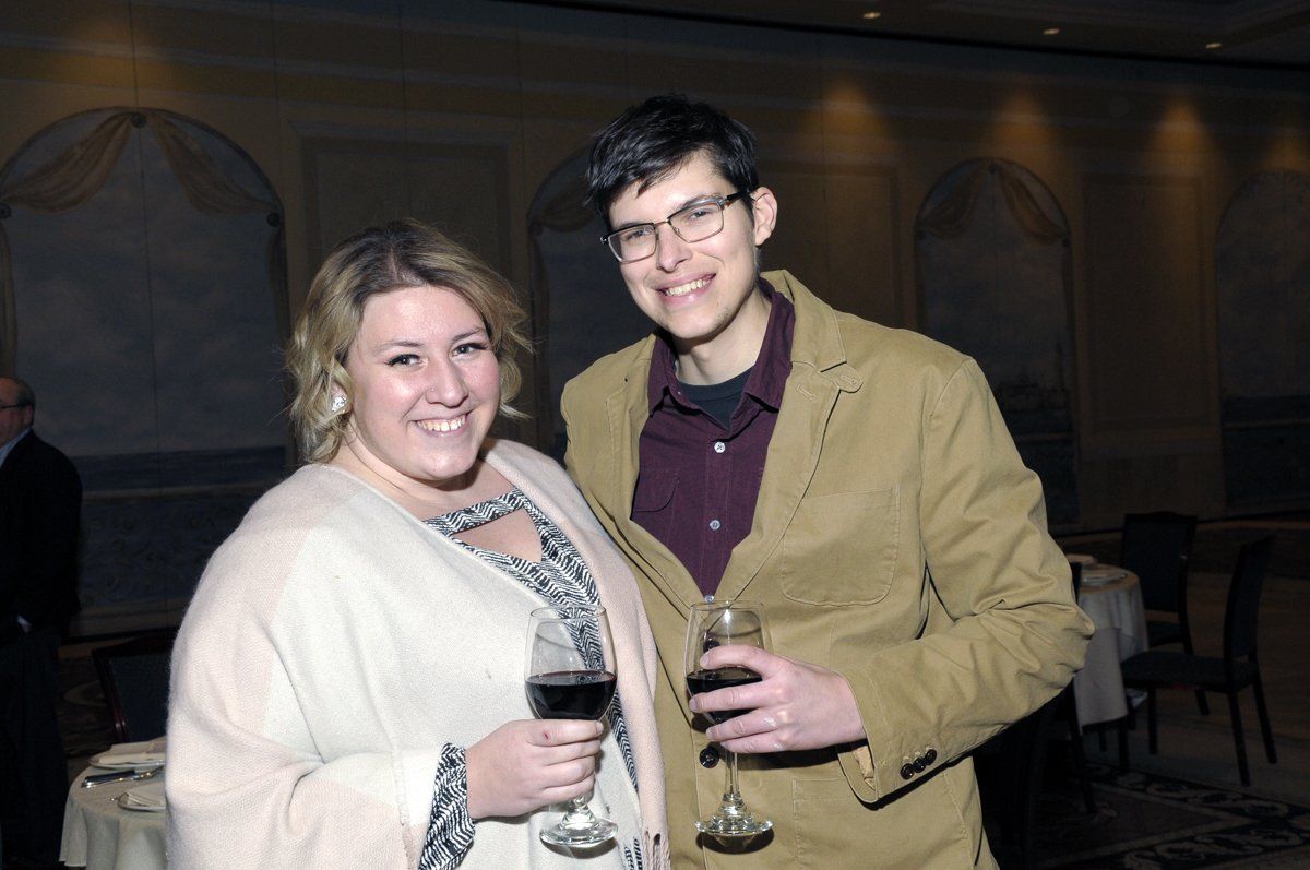 A man and a woman are posing for a picture while holding wine glasses.