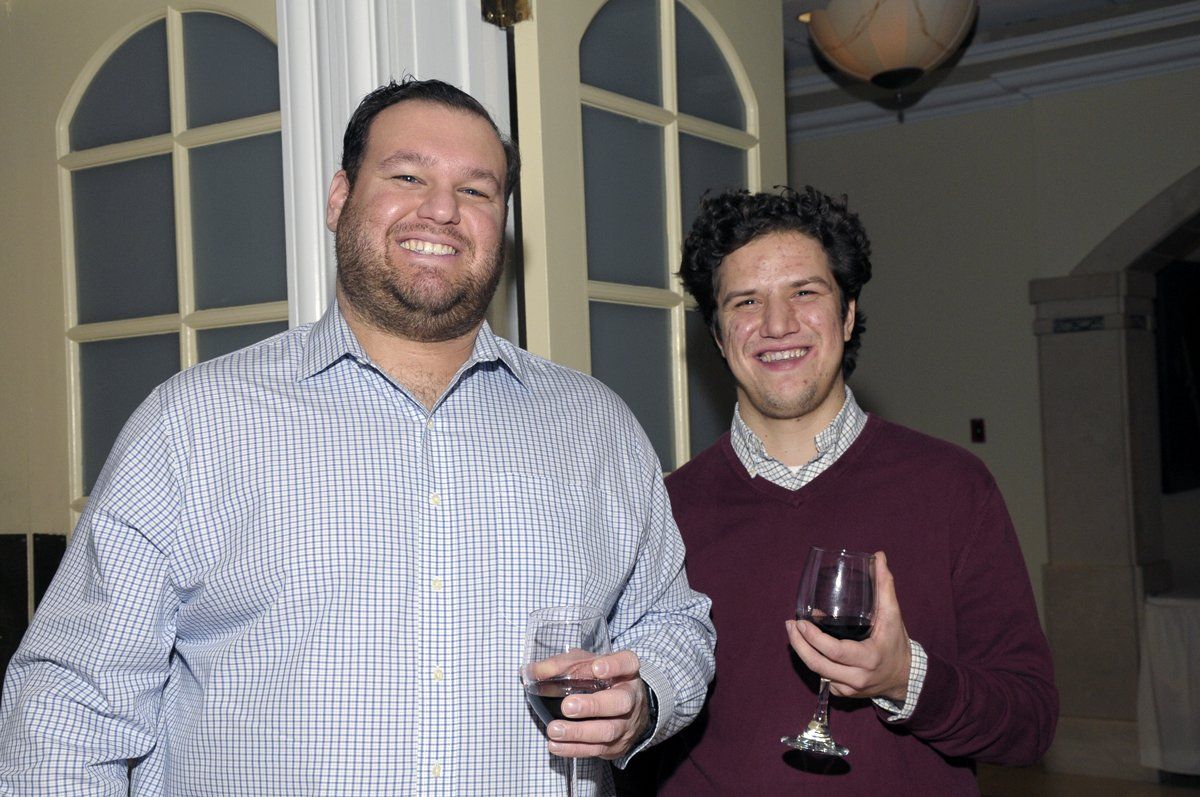 Two men standing next to each other holding wine glasses