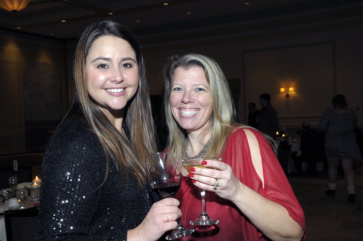 Two women are posing for a picture while holding wine glasses.