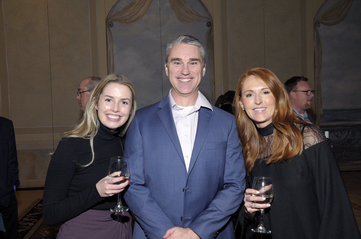 A man and two women are posing for a picture while holding wine glasses.