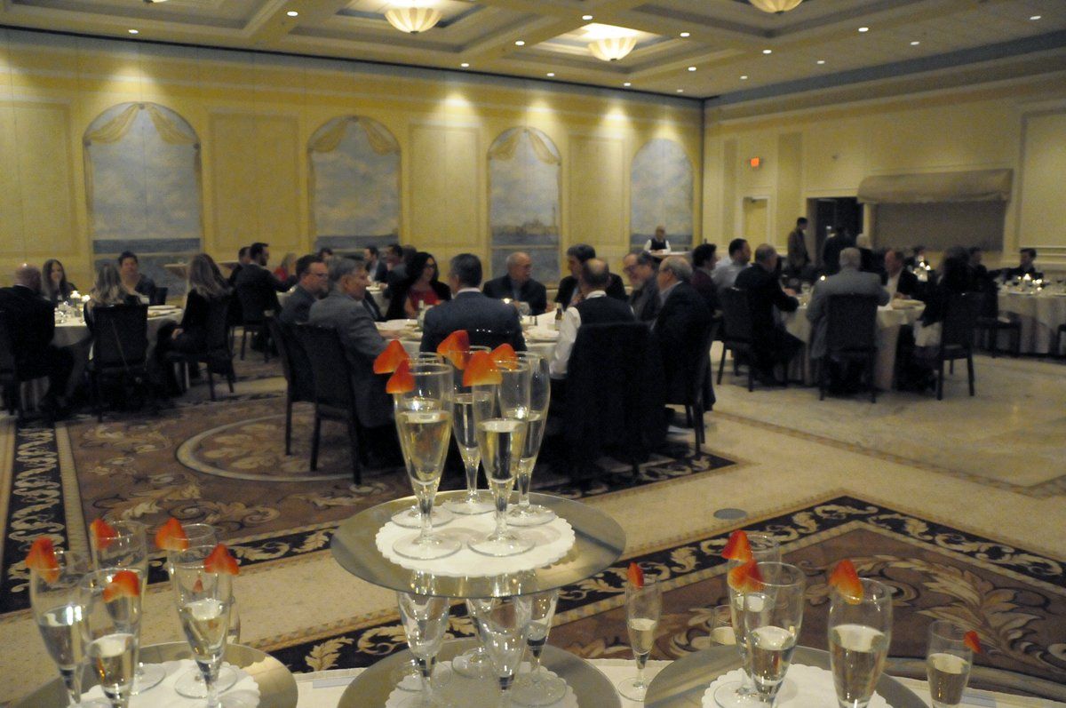 A group of people are sitting at tables in a large room with glasses of champagne on the table