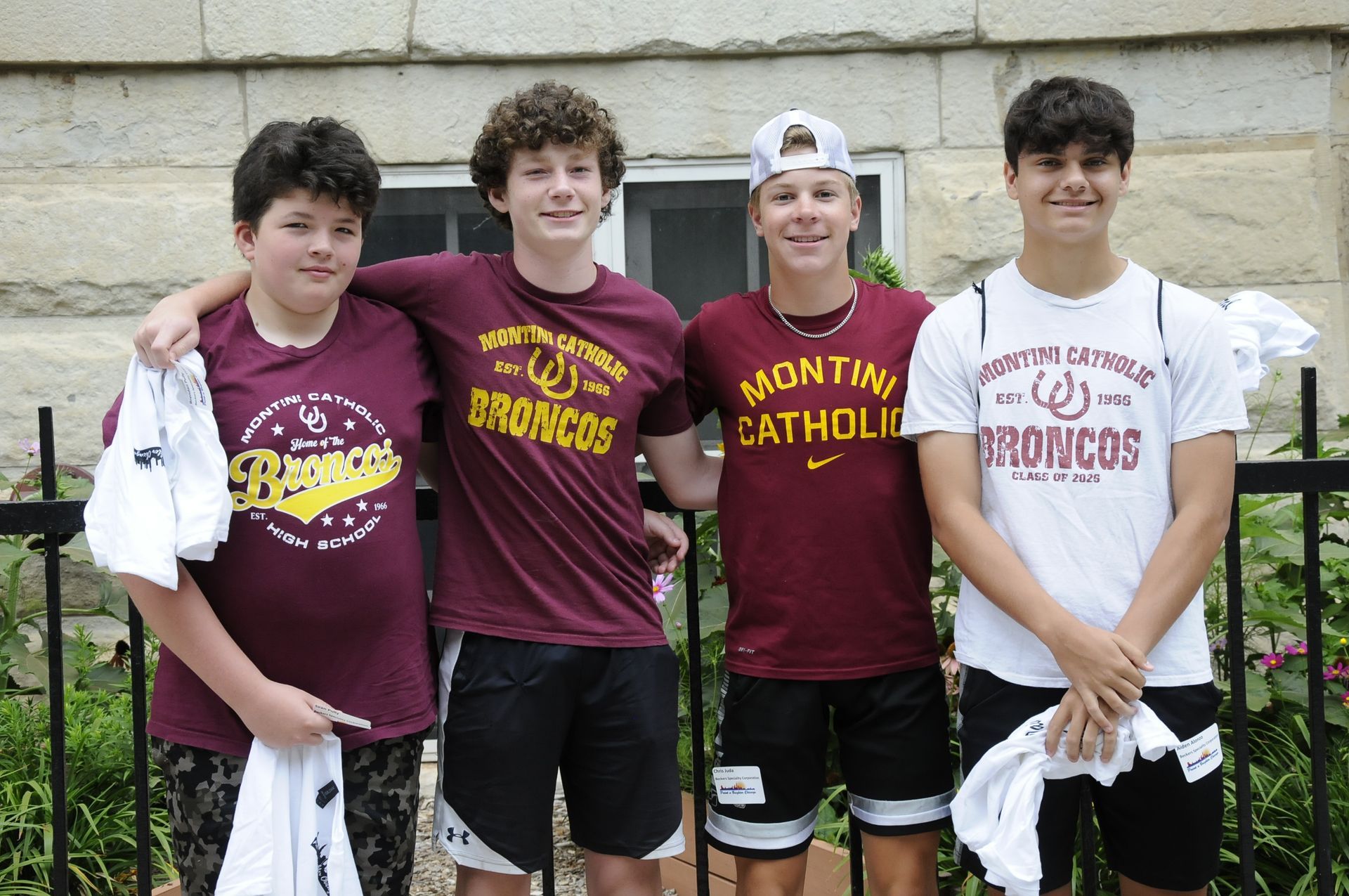 Four boys are posing for a picture and one of them is wearing a shirt that says catholic