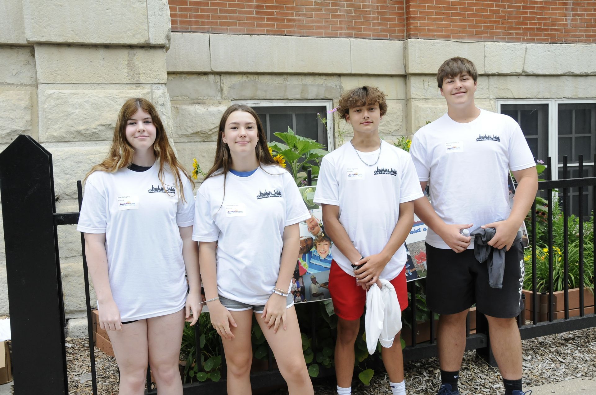 A group of young people are standing next to each other in front of a brick building.