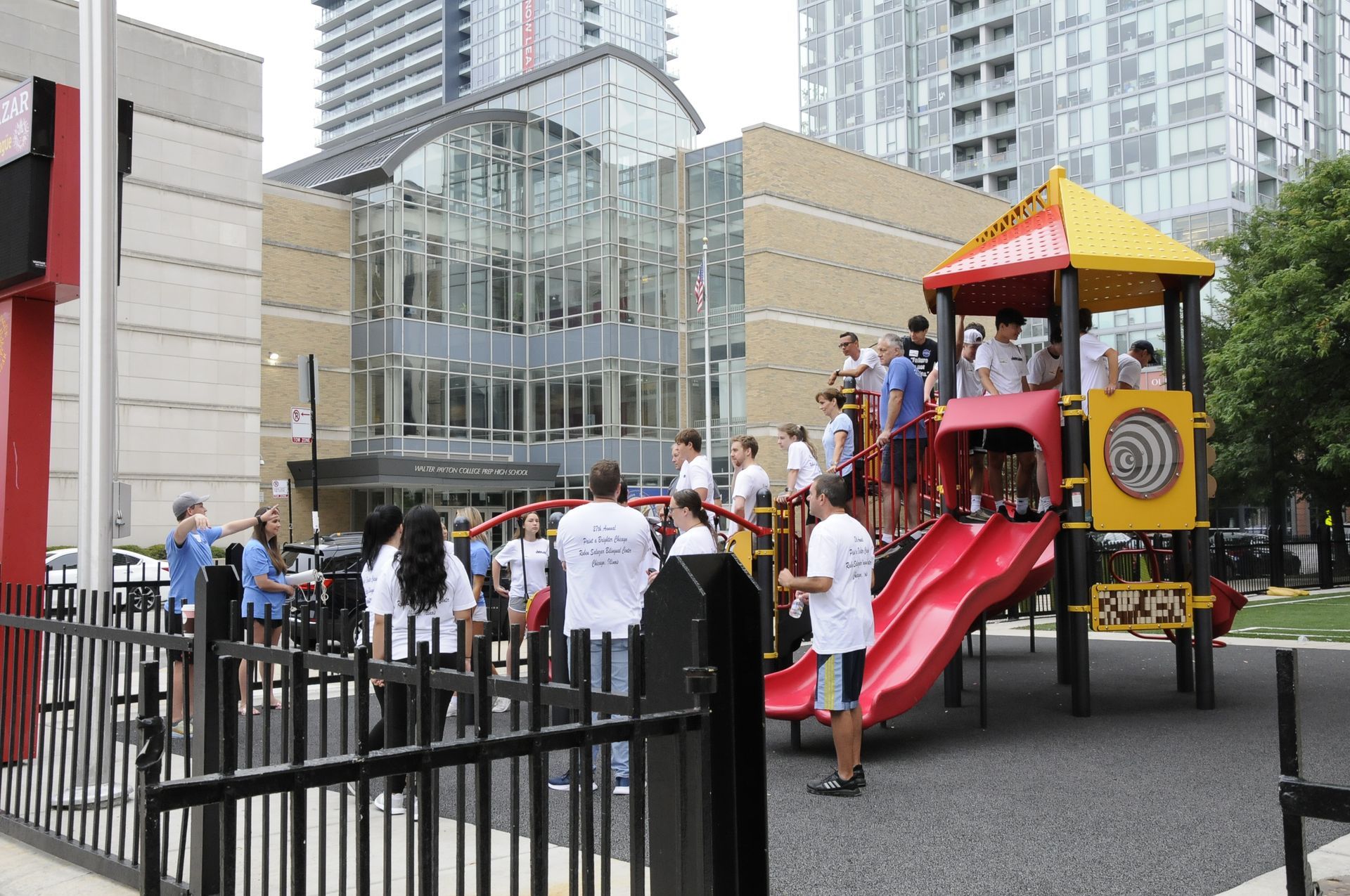 A group of people standing around a playground in front of a building