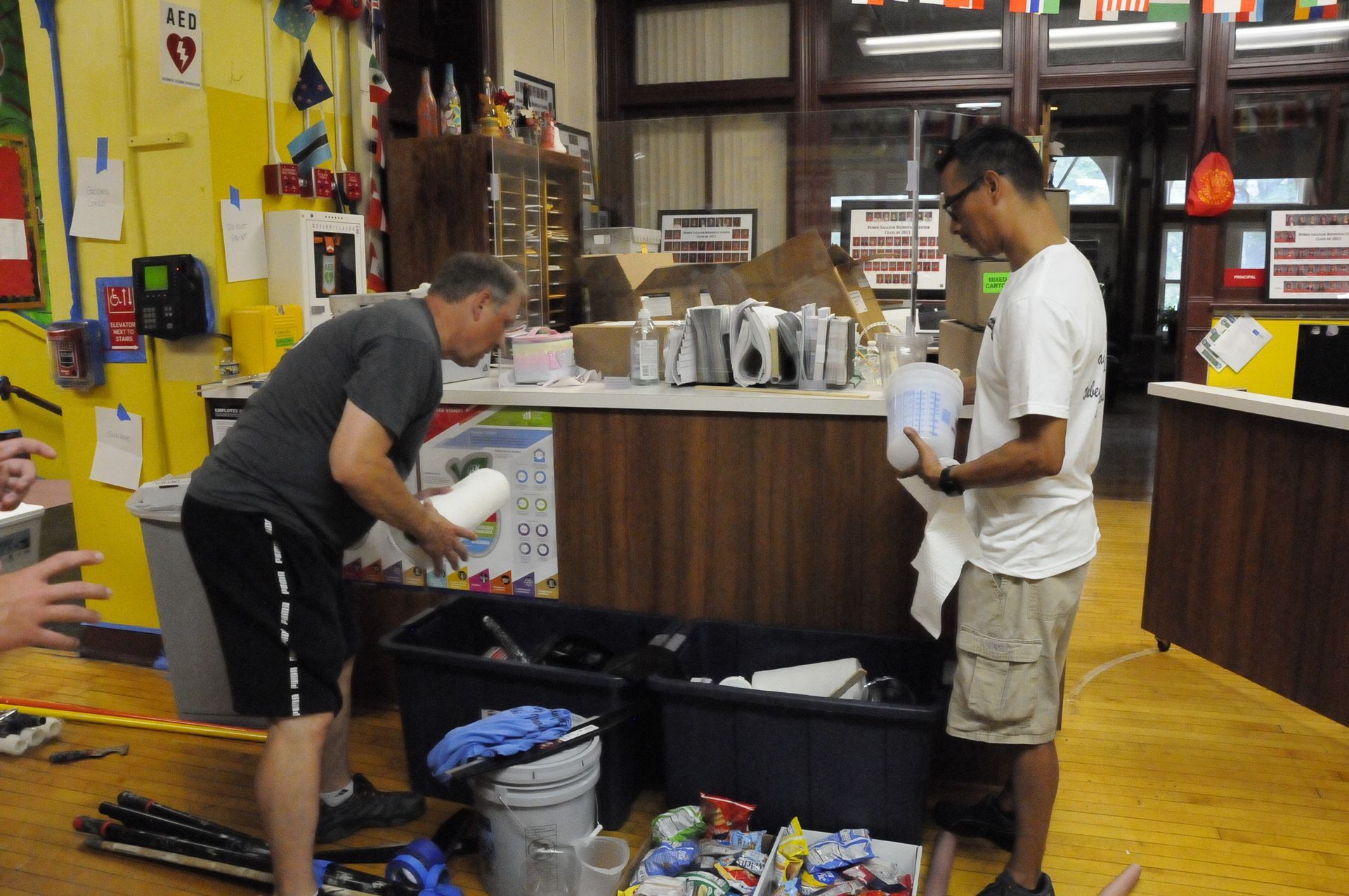 Two men are working on a counter in a messy room