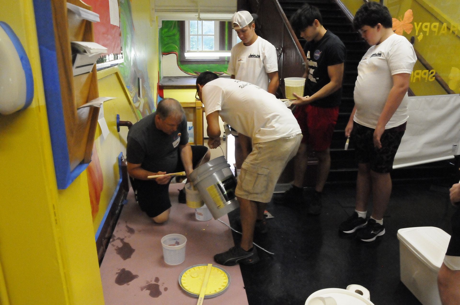 A group of men are painting a wall with yellow paint