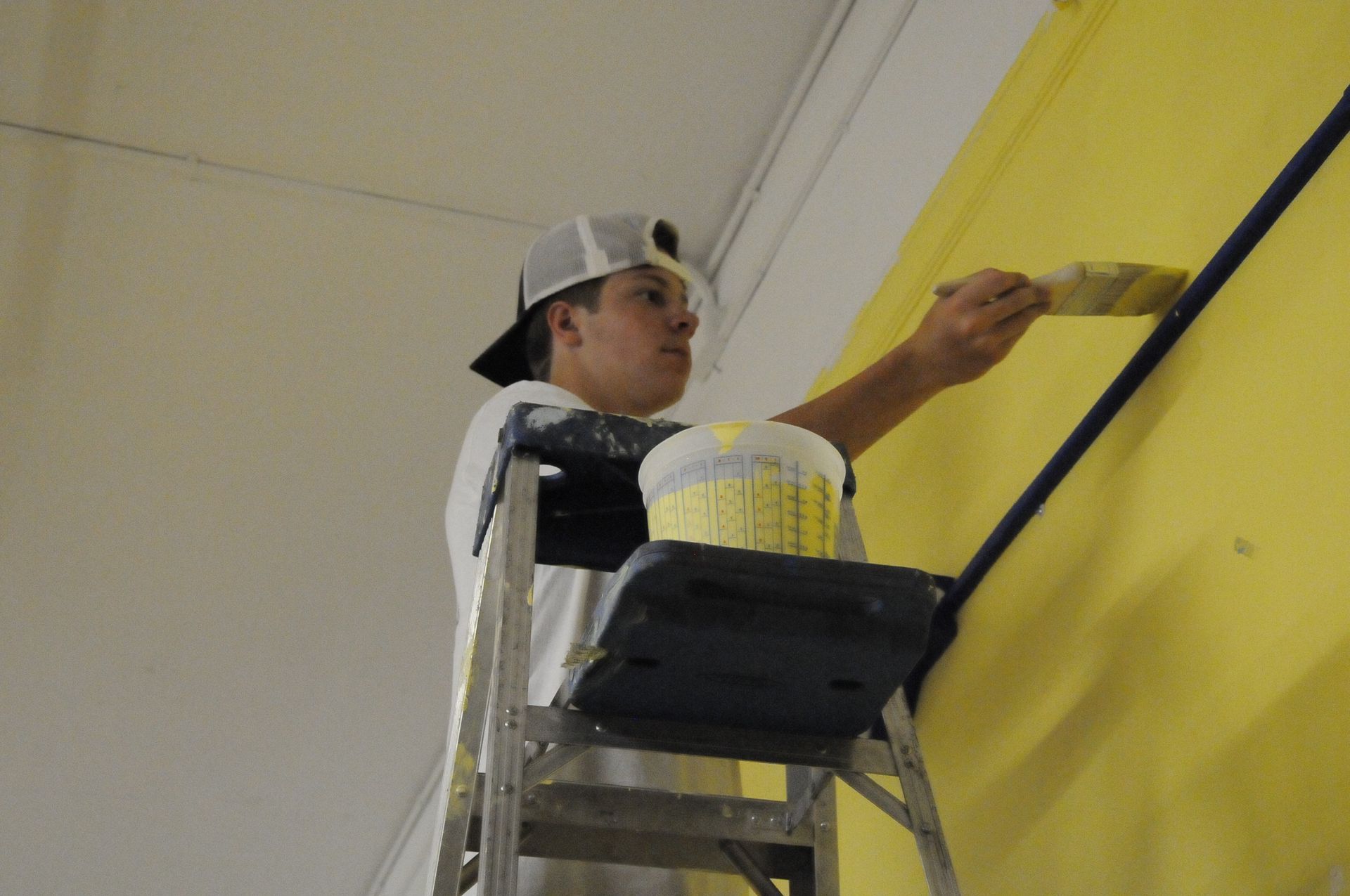 A man on a ladder is painting a yellow wall