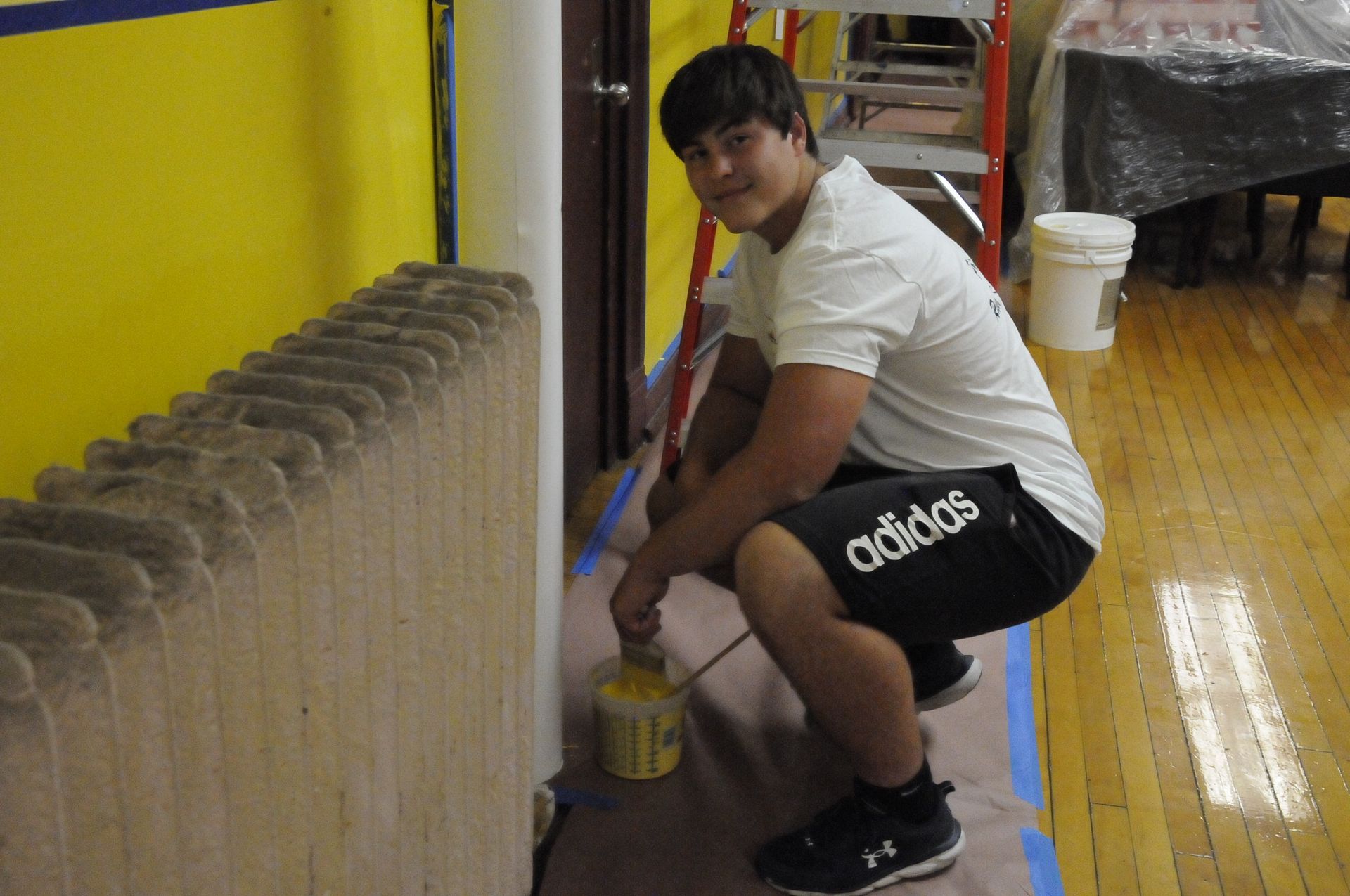 A man wearing adidas shorts is kneeling down and painting a wall