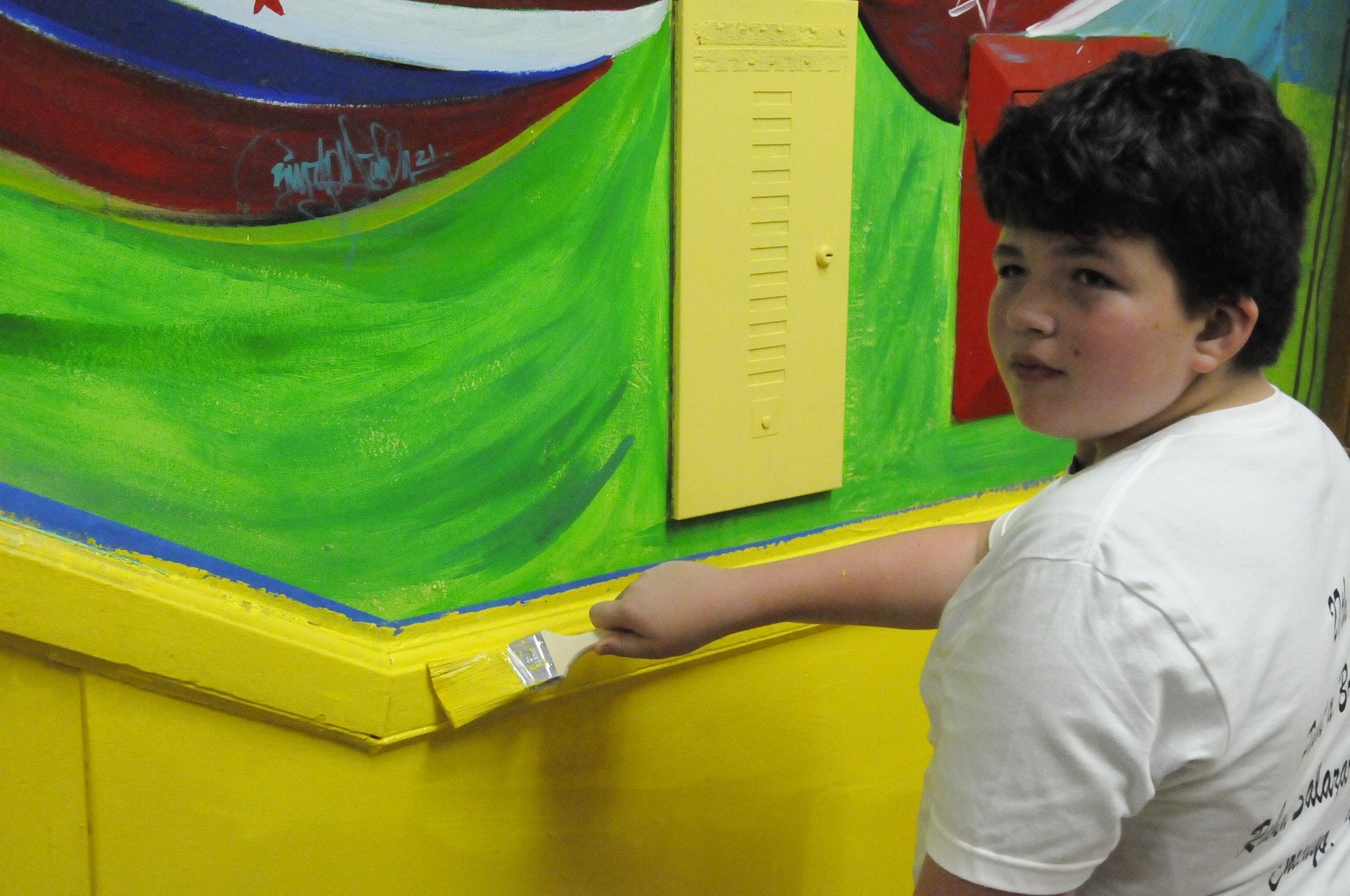 A young boy in a white shirt is painting a wall