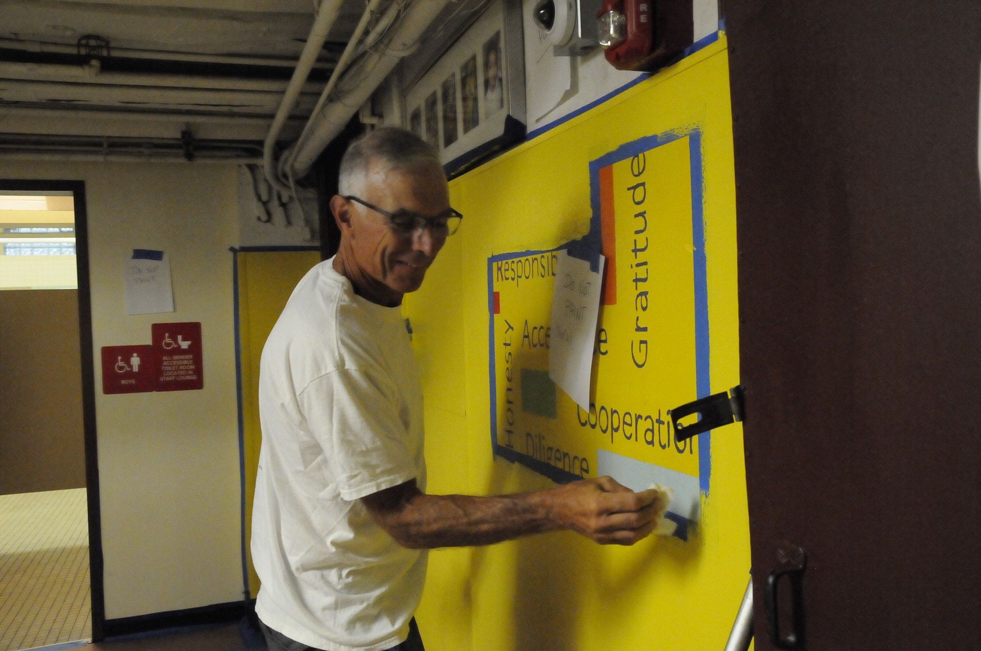 A man in a white shirt is working on a yellow wall