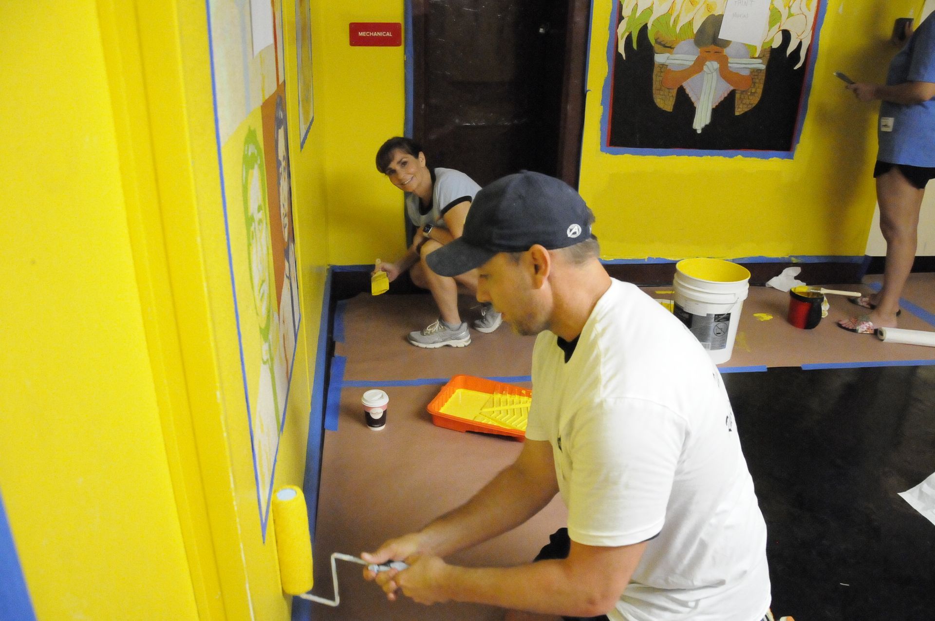A man is painting a yellow wall with a roller