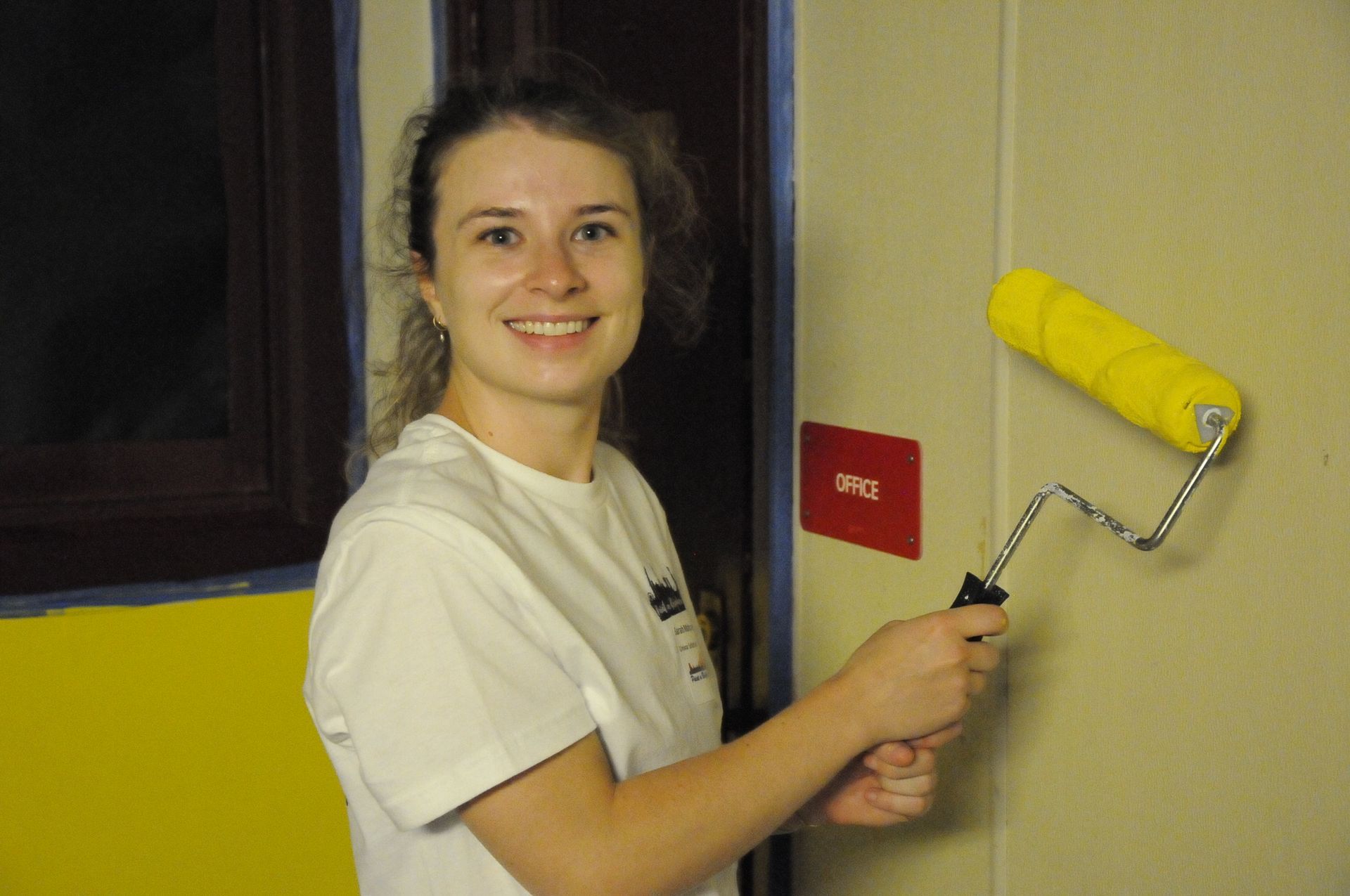 A woman paints a wall with a yellow roller