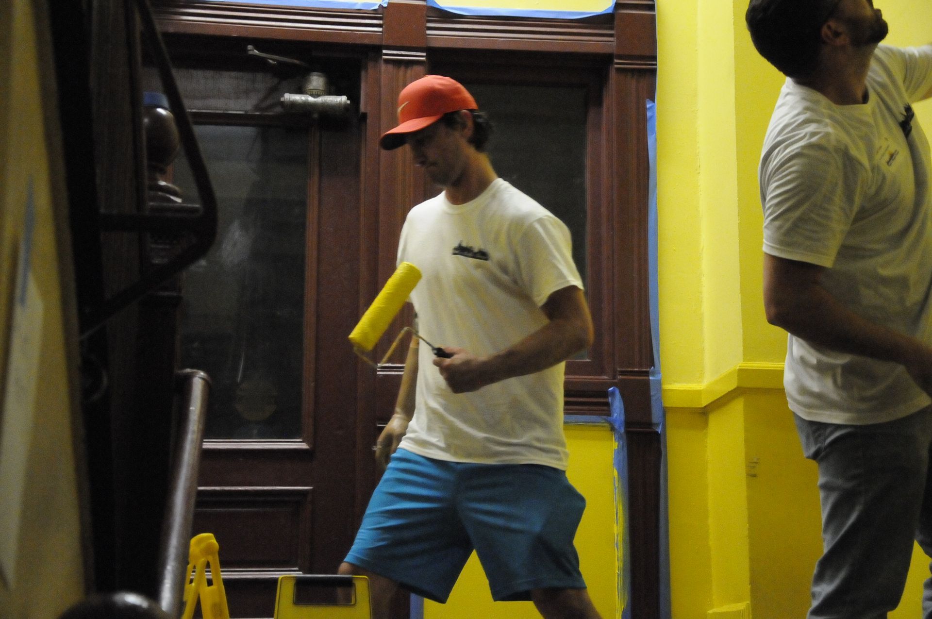 Two men are painting yellow walls and one is holding a yellow roller