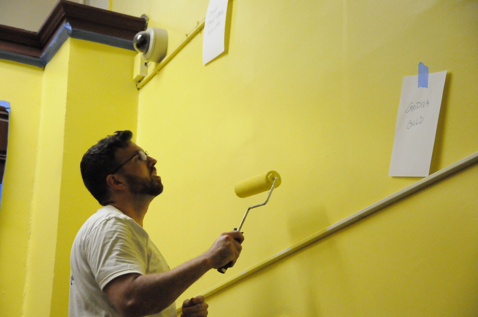 A man is painting a yellow wall with a roller