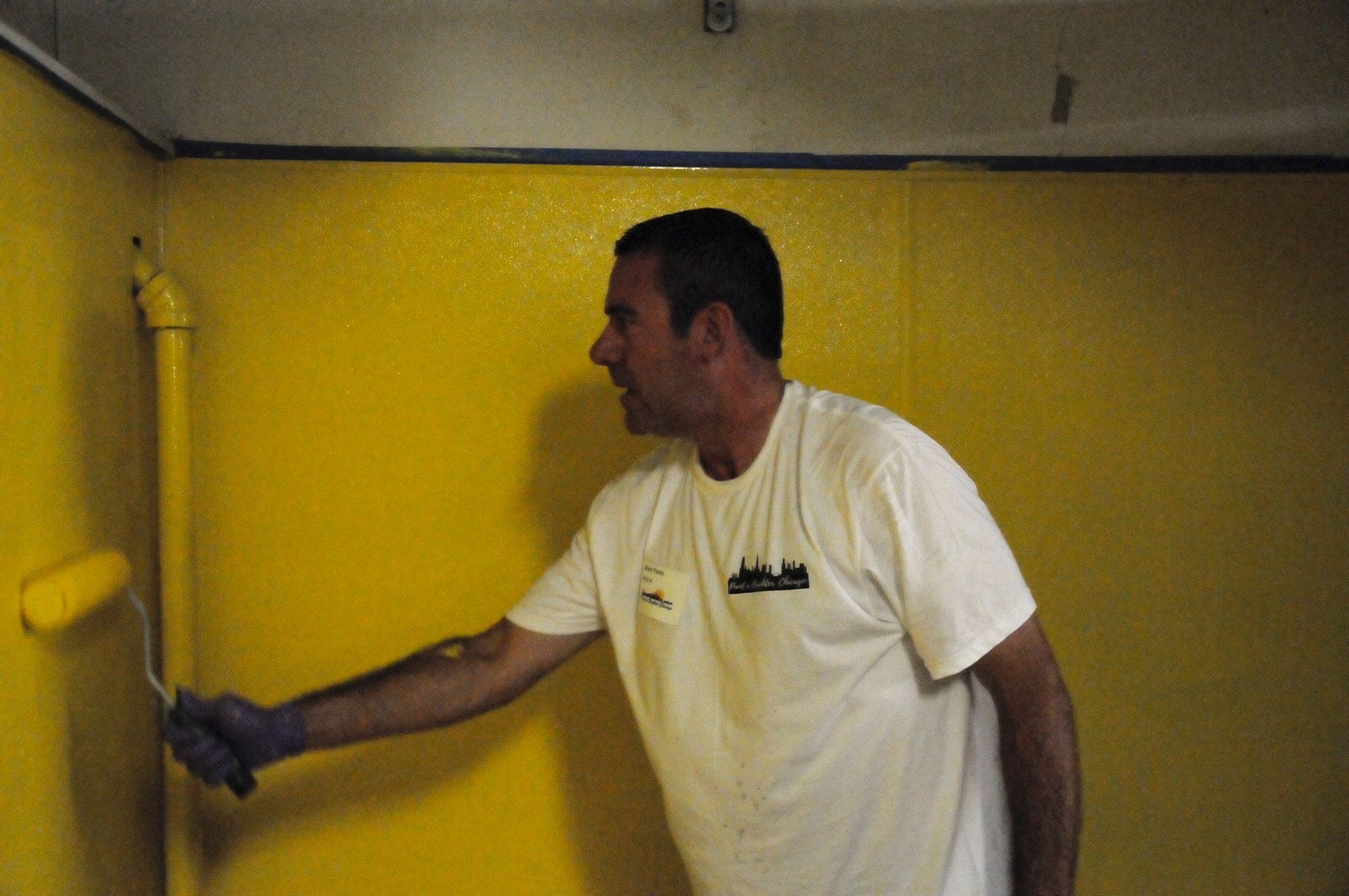 A man is painting a yellow wall with a roller