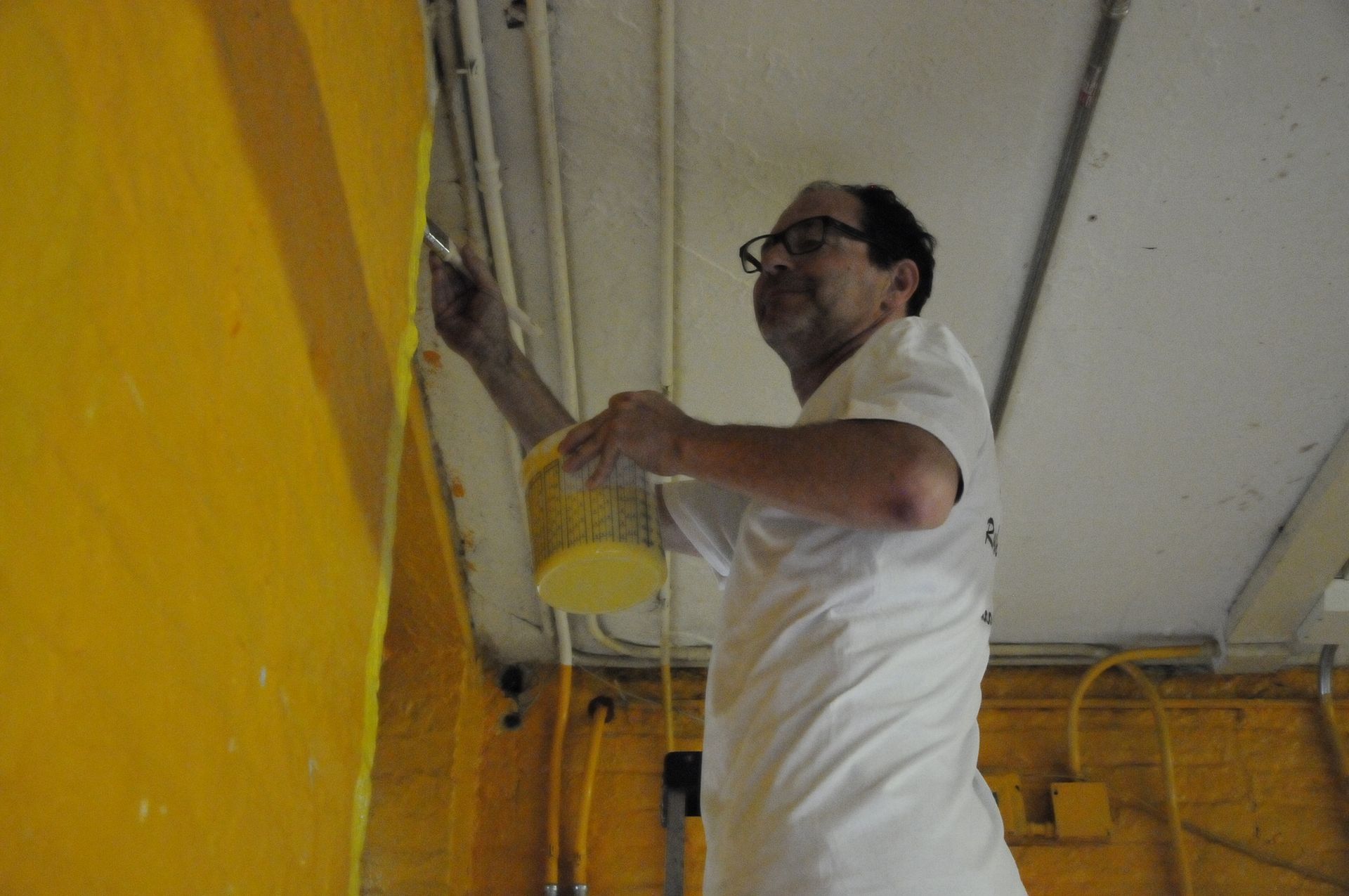 A man is painting a yellow wall with a brush.