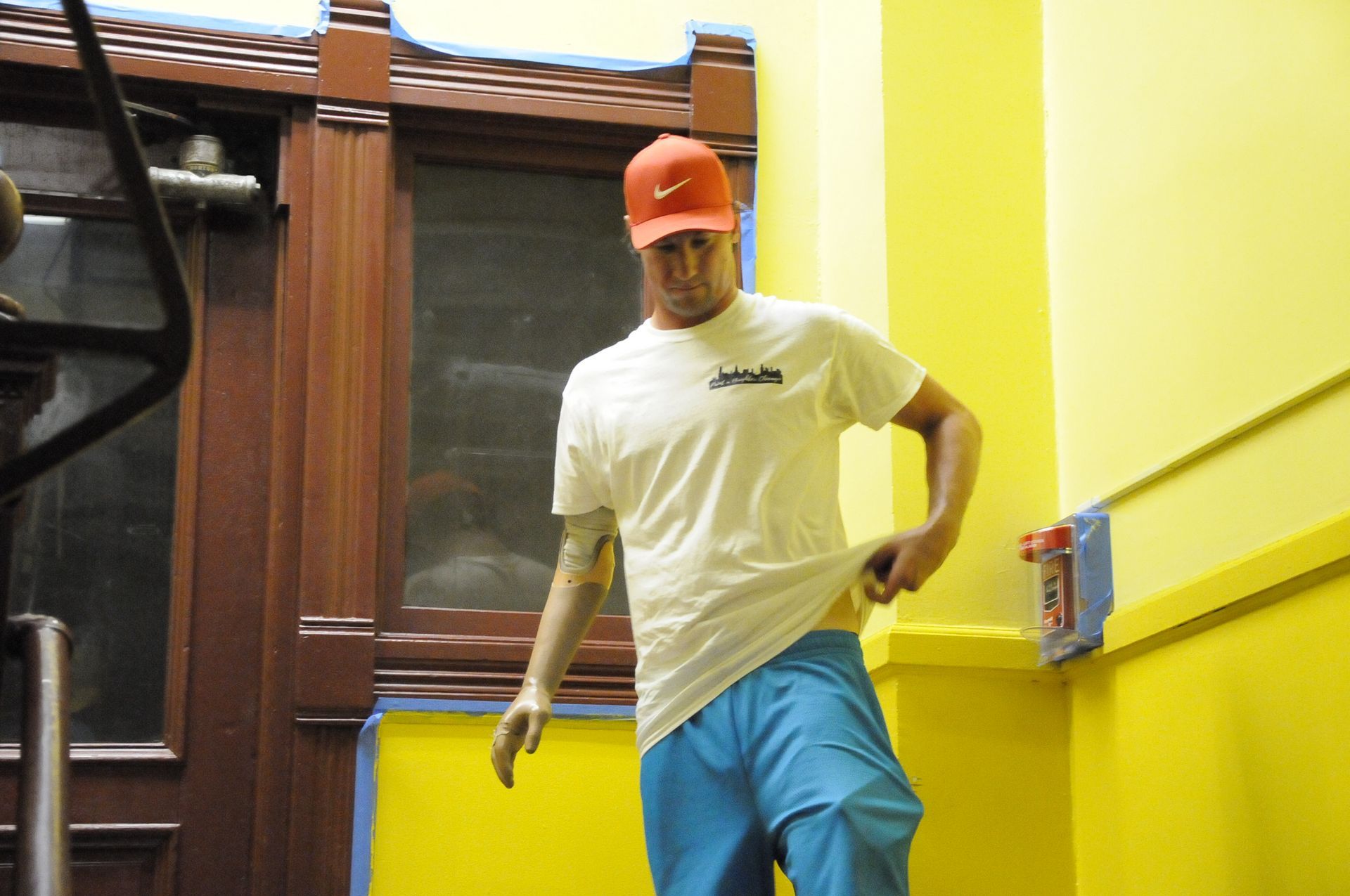 A man wearing a white shirt and a red hat is standing in front of a yellow wall