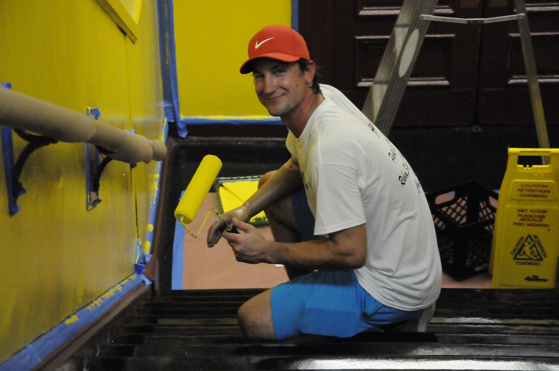 A man in a red hat is kneeling down and painting a wall