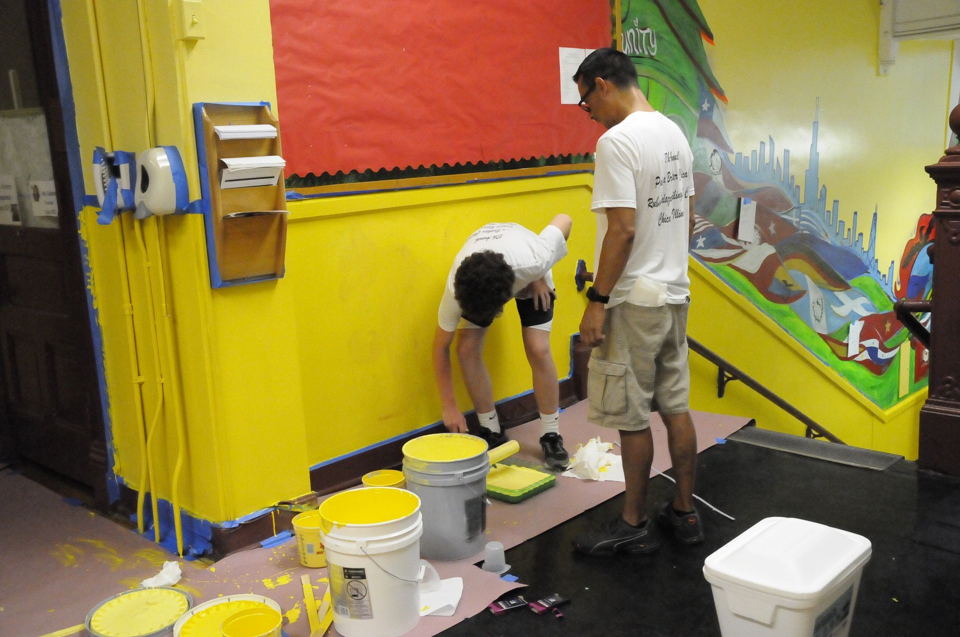 Two men are painting a wall with yellow paint