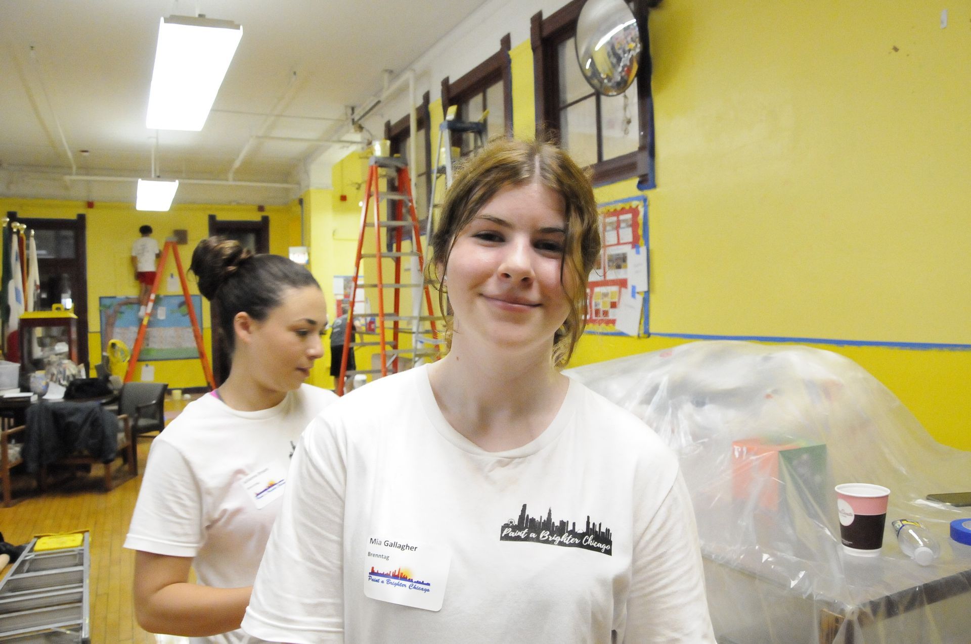 A woman in a white shirt is smiling in a room with yellow walls.