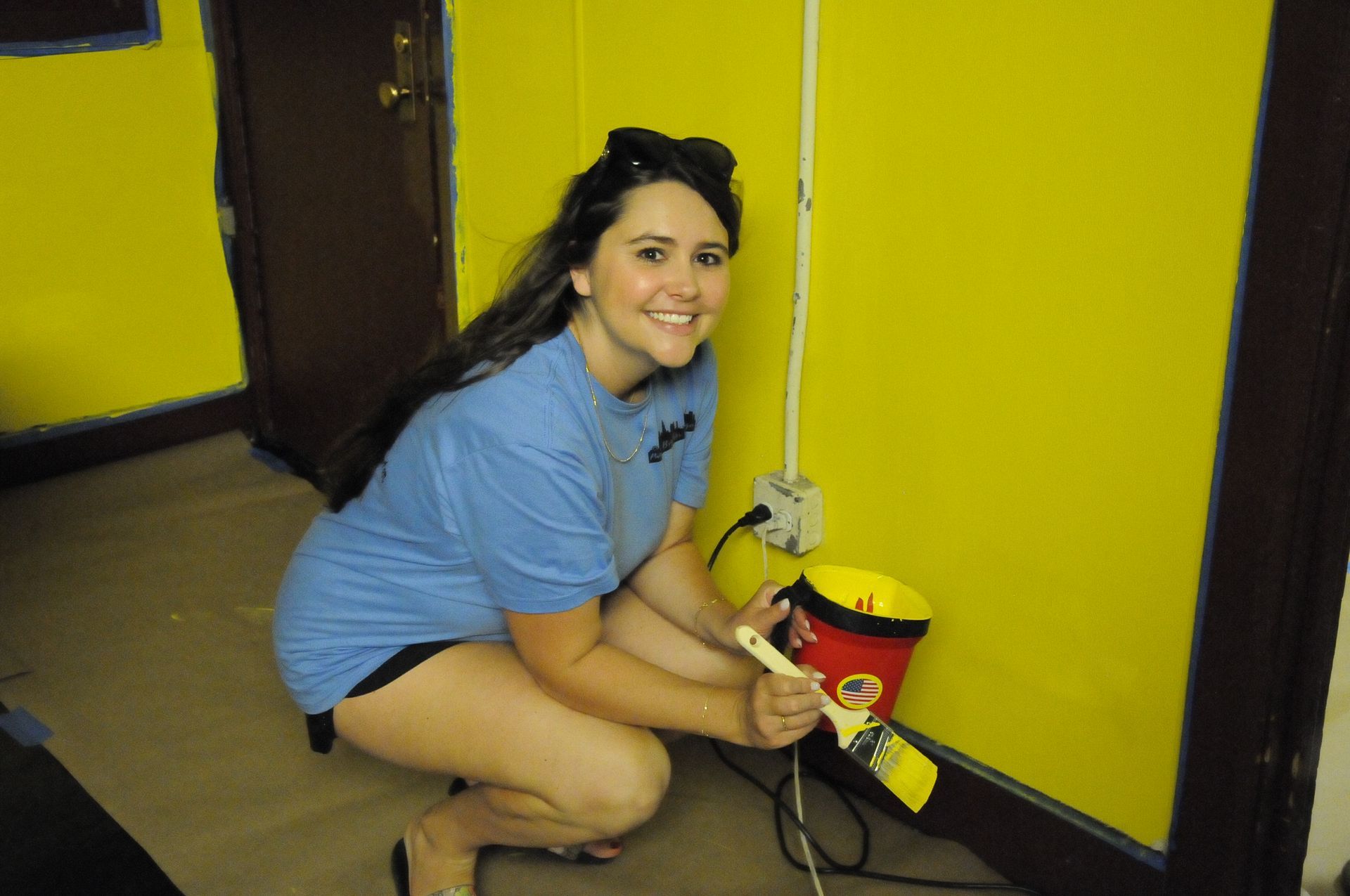 A woman in a blue shirt is painting a yellow wall