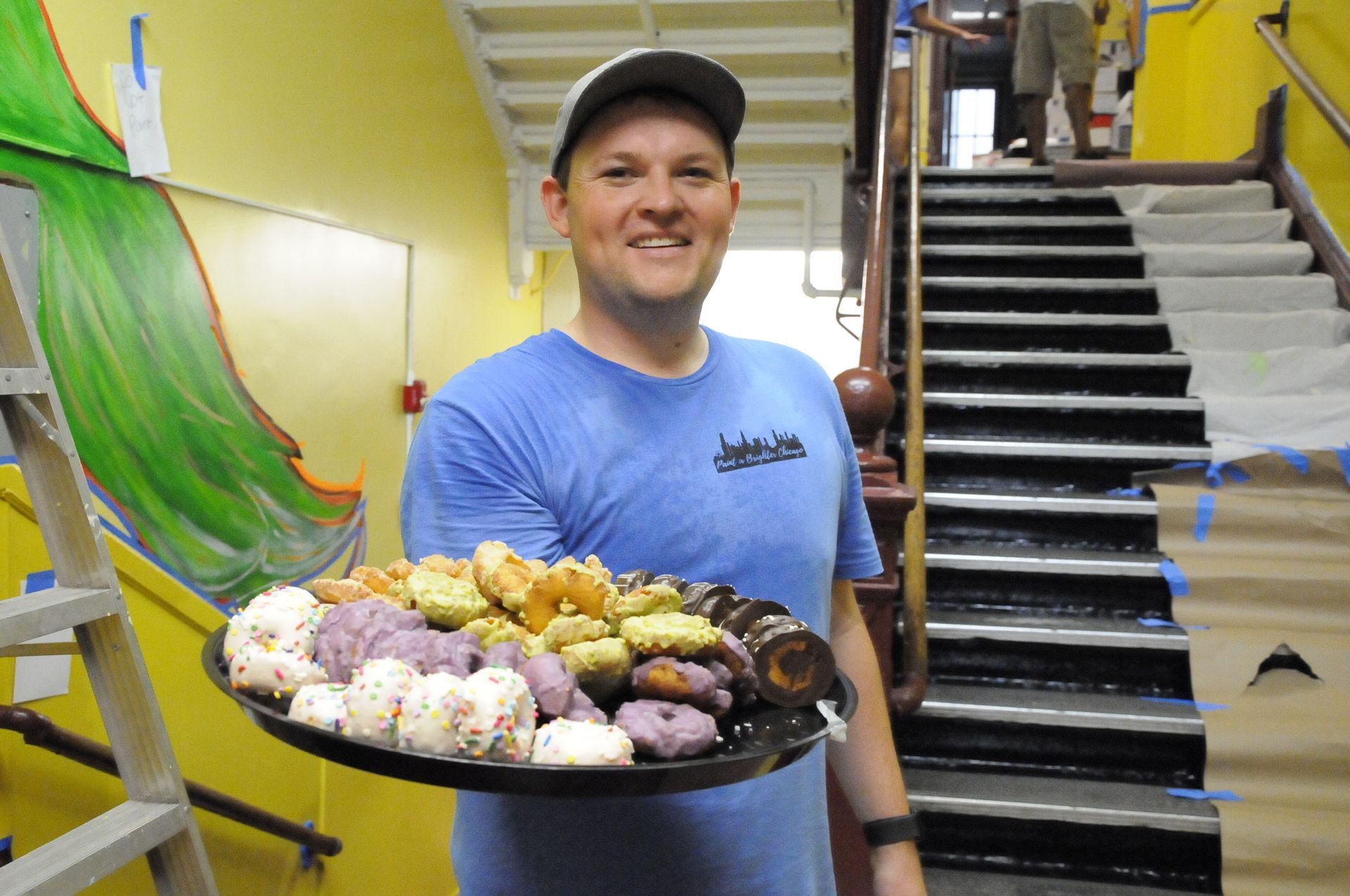 A man in a blue shirt is holding a tray of donuts.