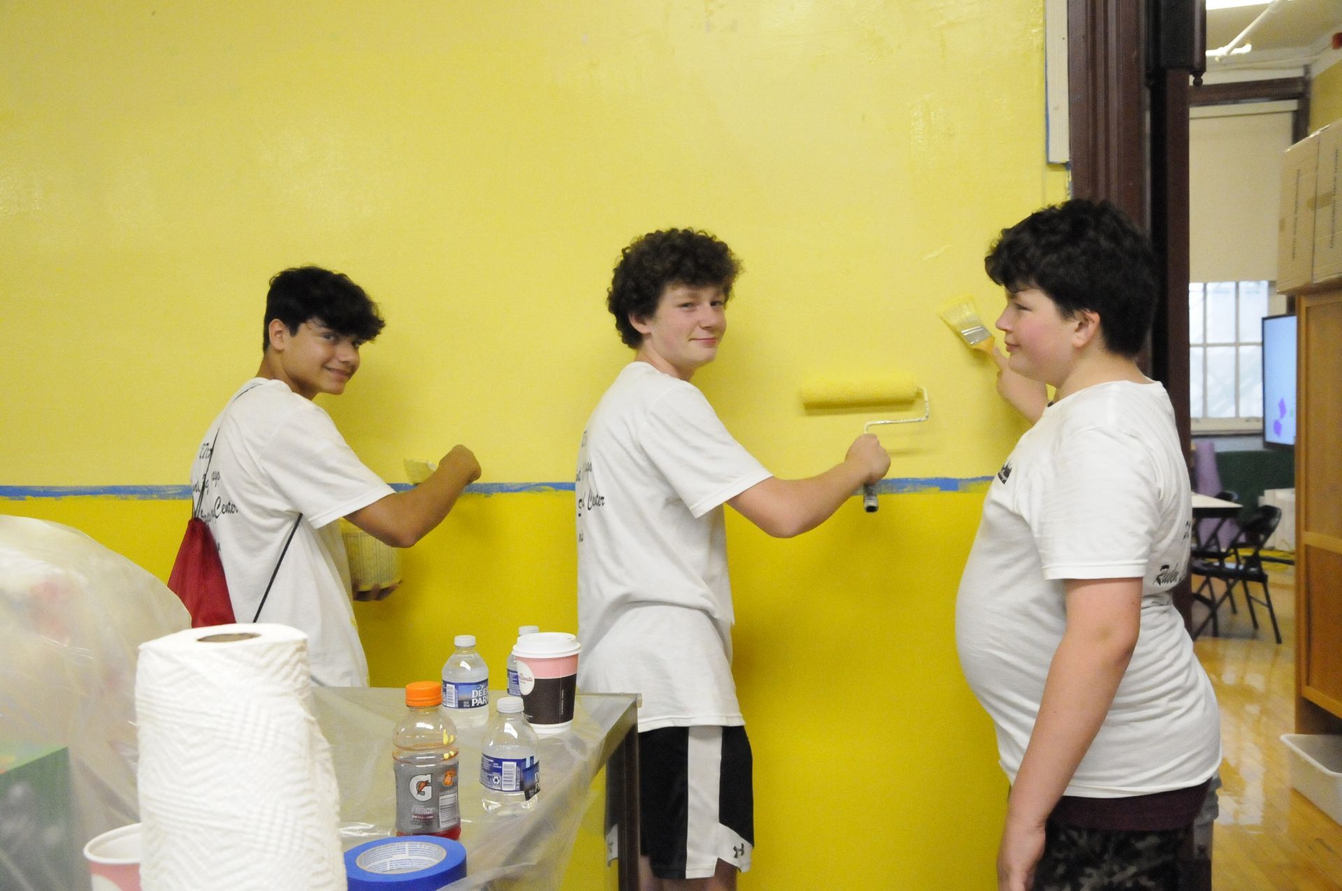 Three boys are painting a yellow wall together