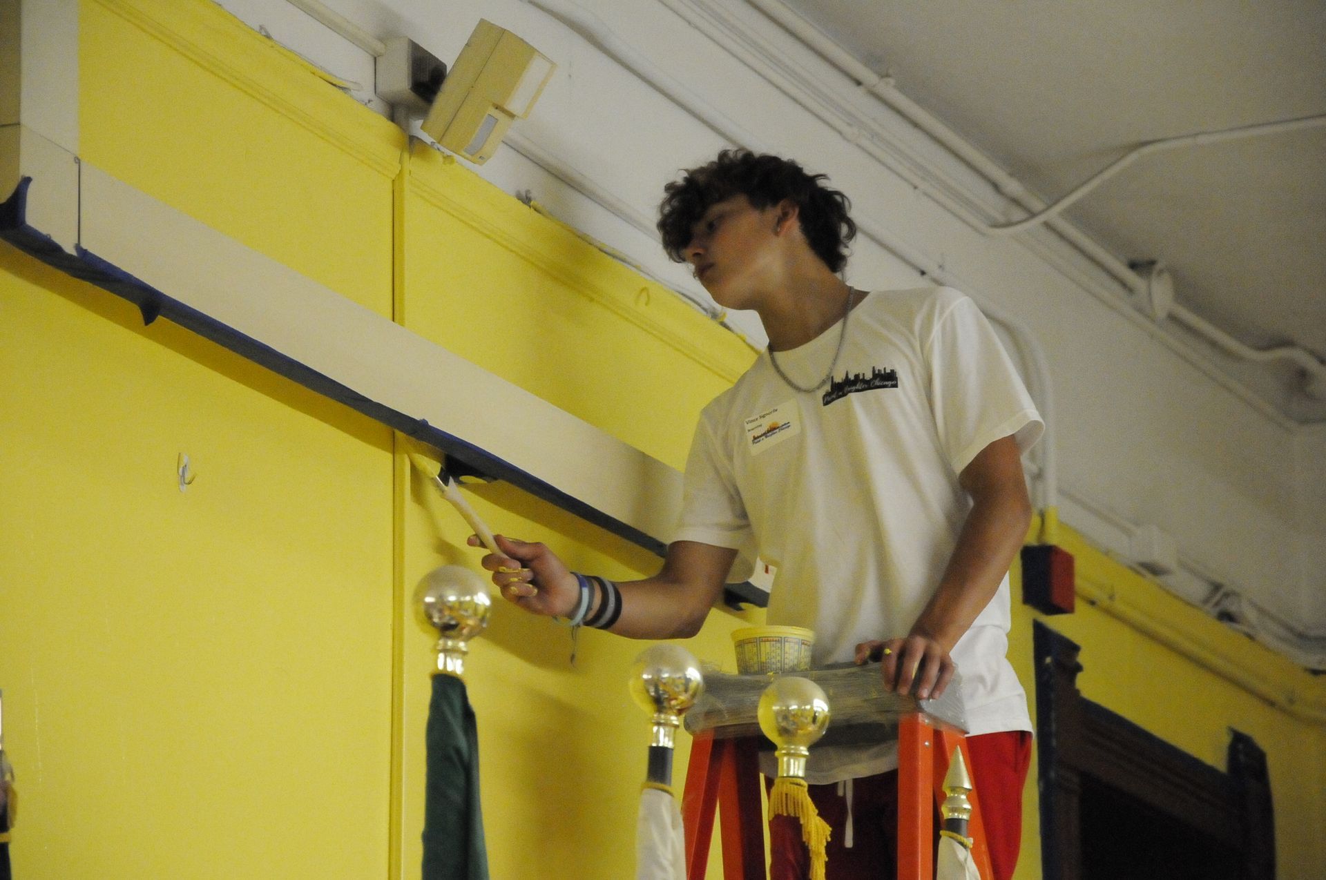 A man in a white adidas shirt is painting a yellow wall