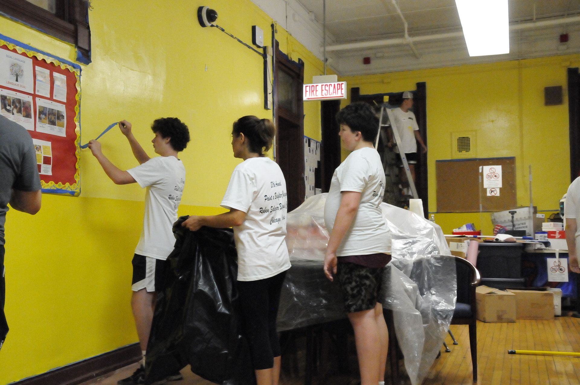 A group of people are working in a room with an exit sign above them