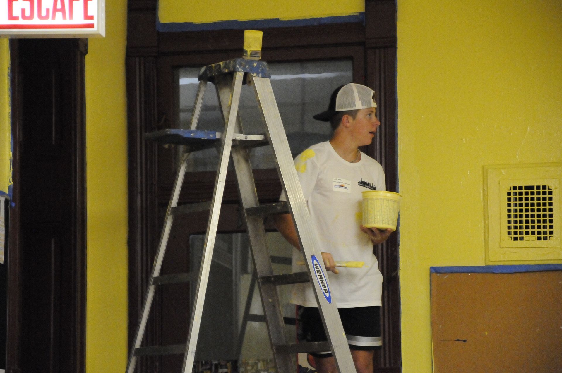 A man standing on a ladder painting a yellow wall