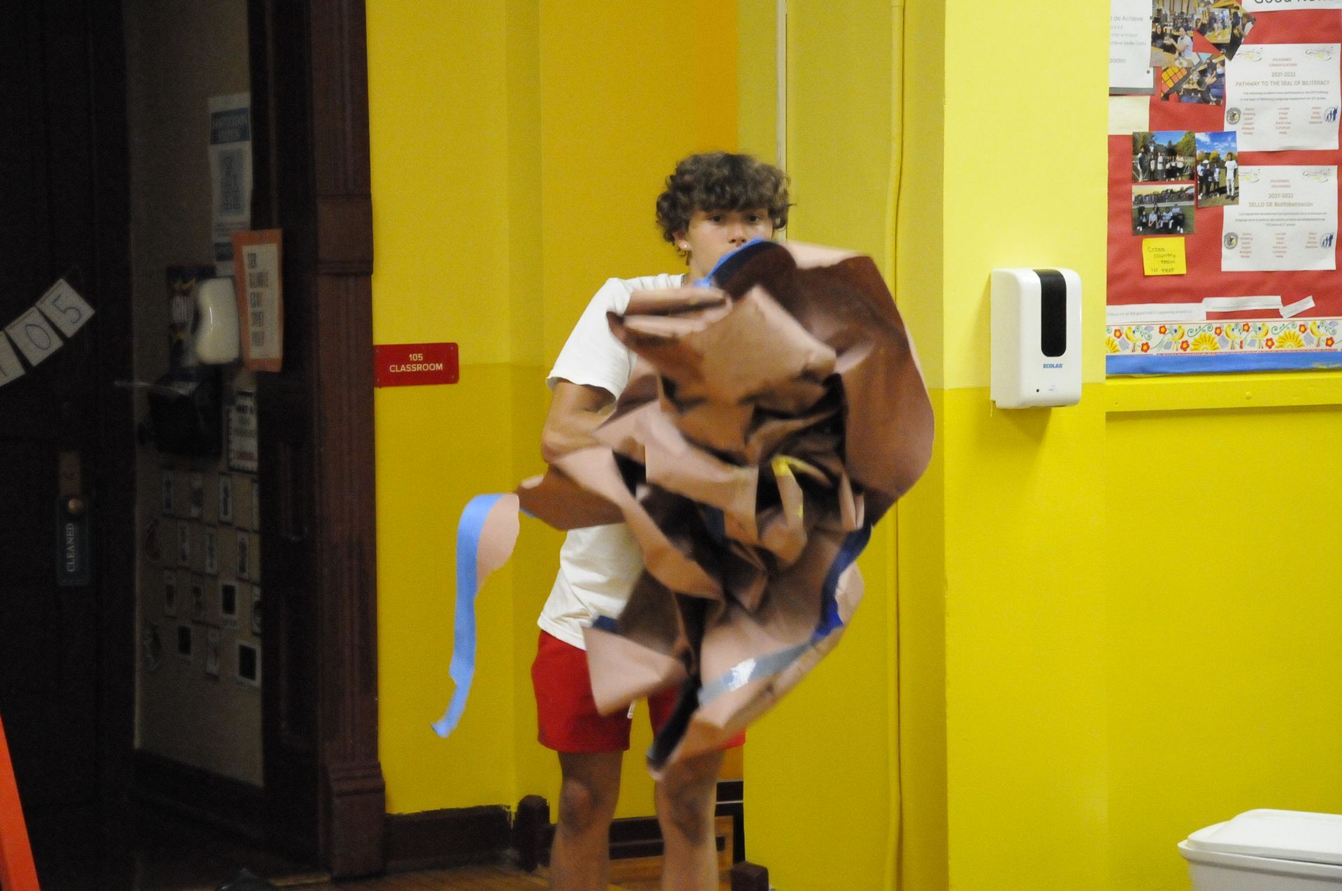 A young boy is holding a large piece of paper in a yellow room.