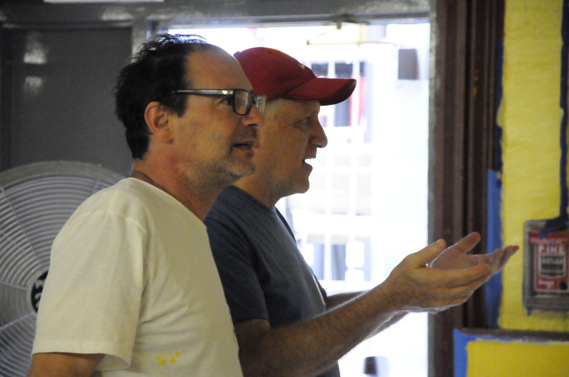 Two men standing next to each other with one wearing a red hat