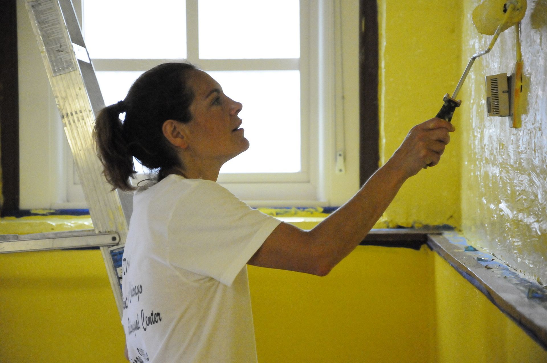 A woman is painting a yellow wall with a roller