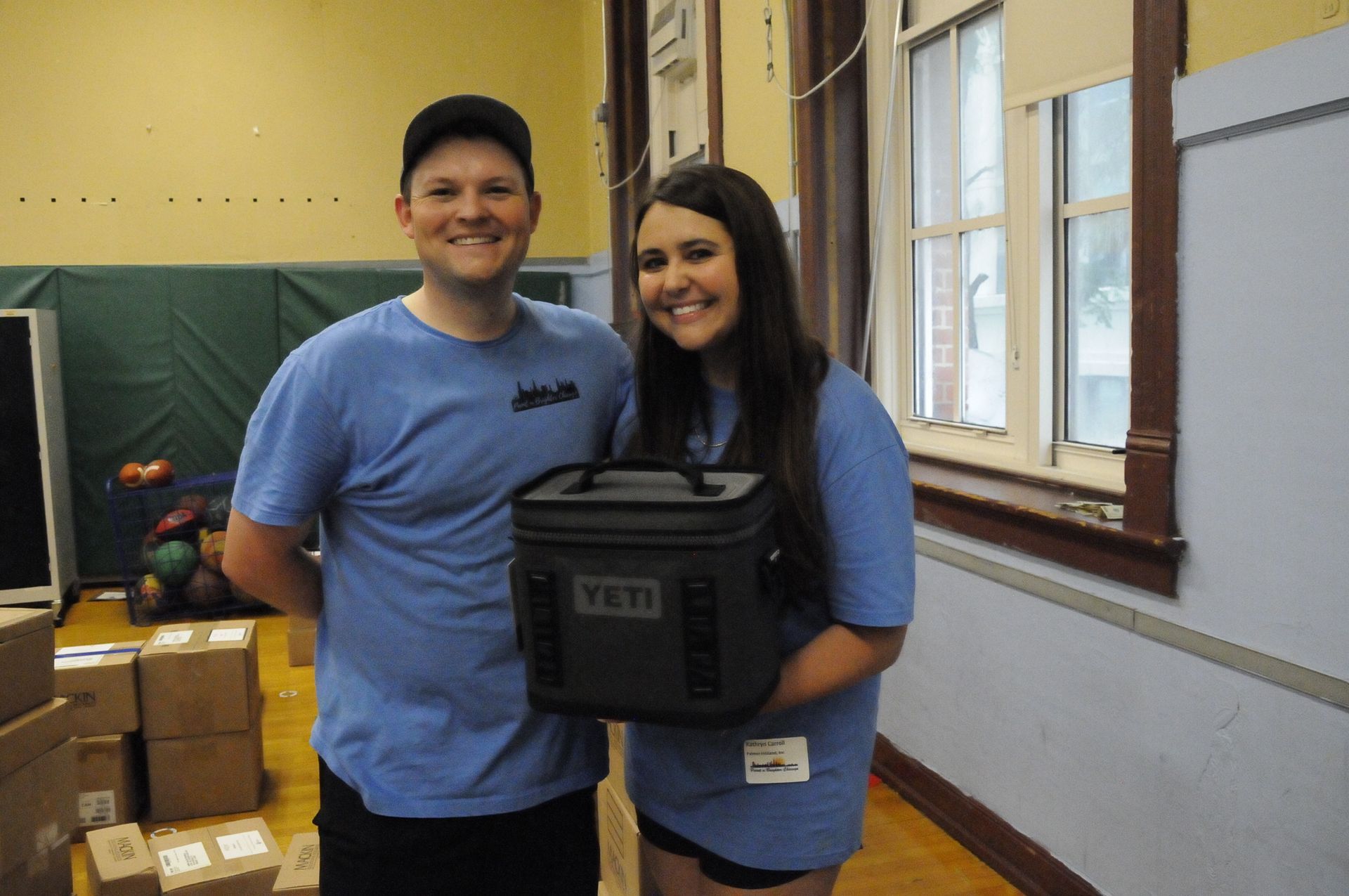 A man and a woman are standing next to each other holding a yeti cooler.