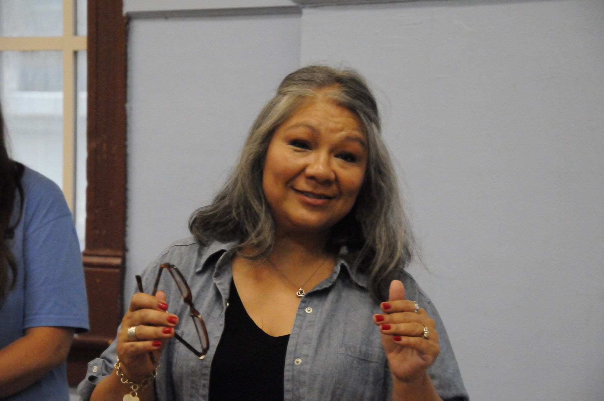A woman is holding a pair of glasses and smiling.