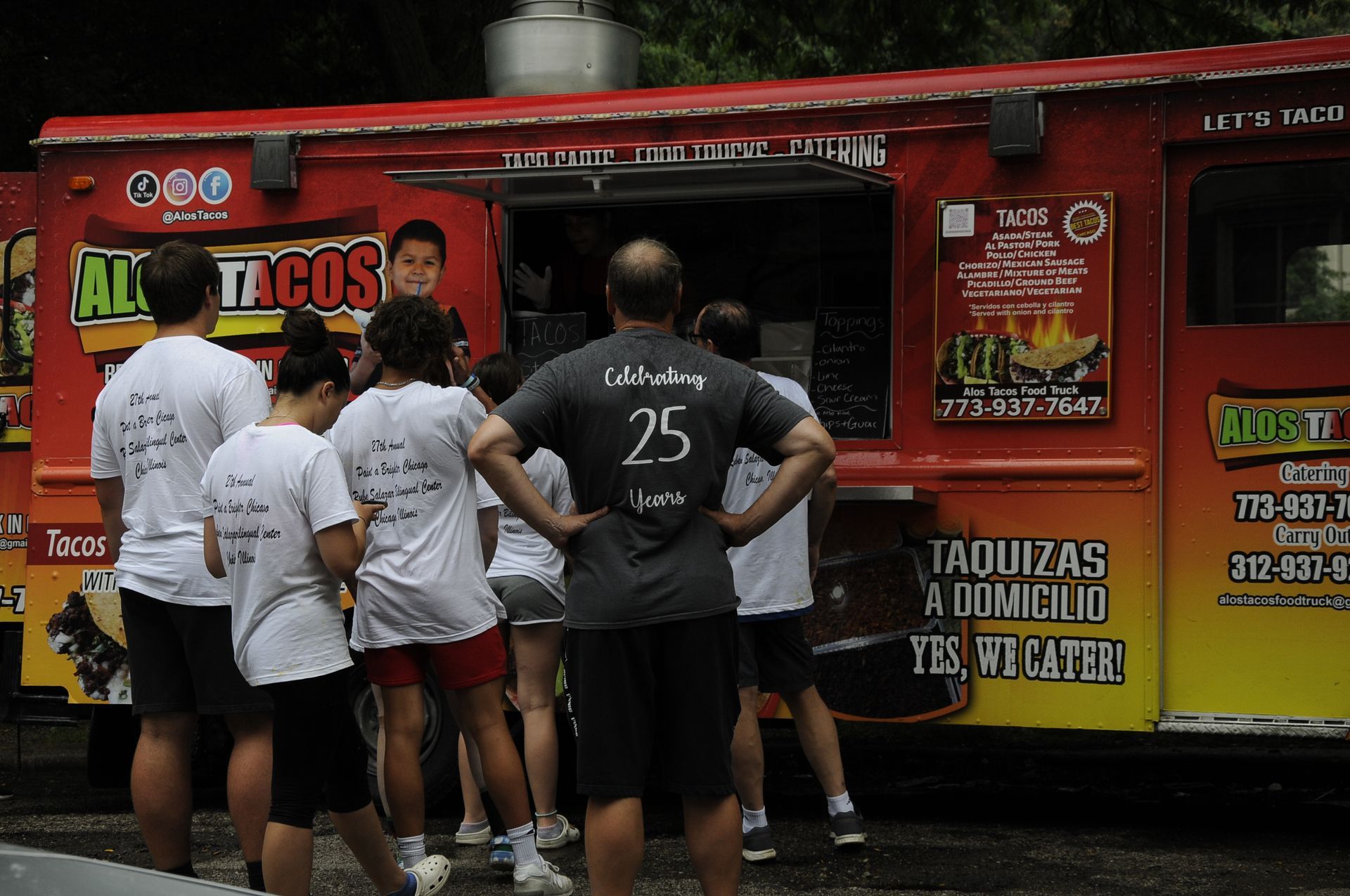 A group of people standing in front of a tacos truck