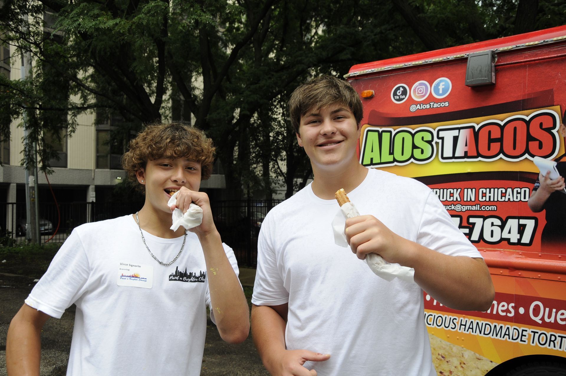 Two young men eating tacos in front of a food truck that says alos tacos