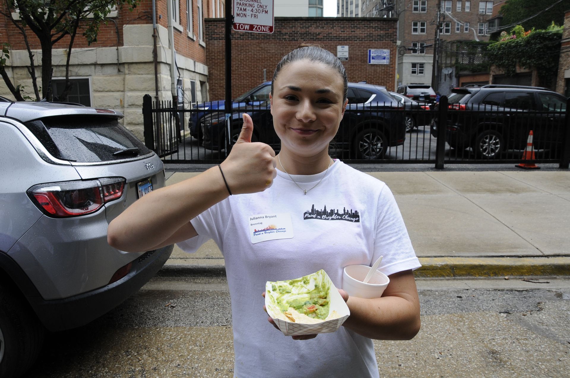 A woman in a white shirt is giving a thumbs up while holding a taco.