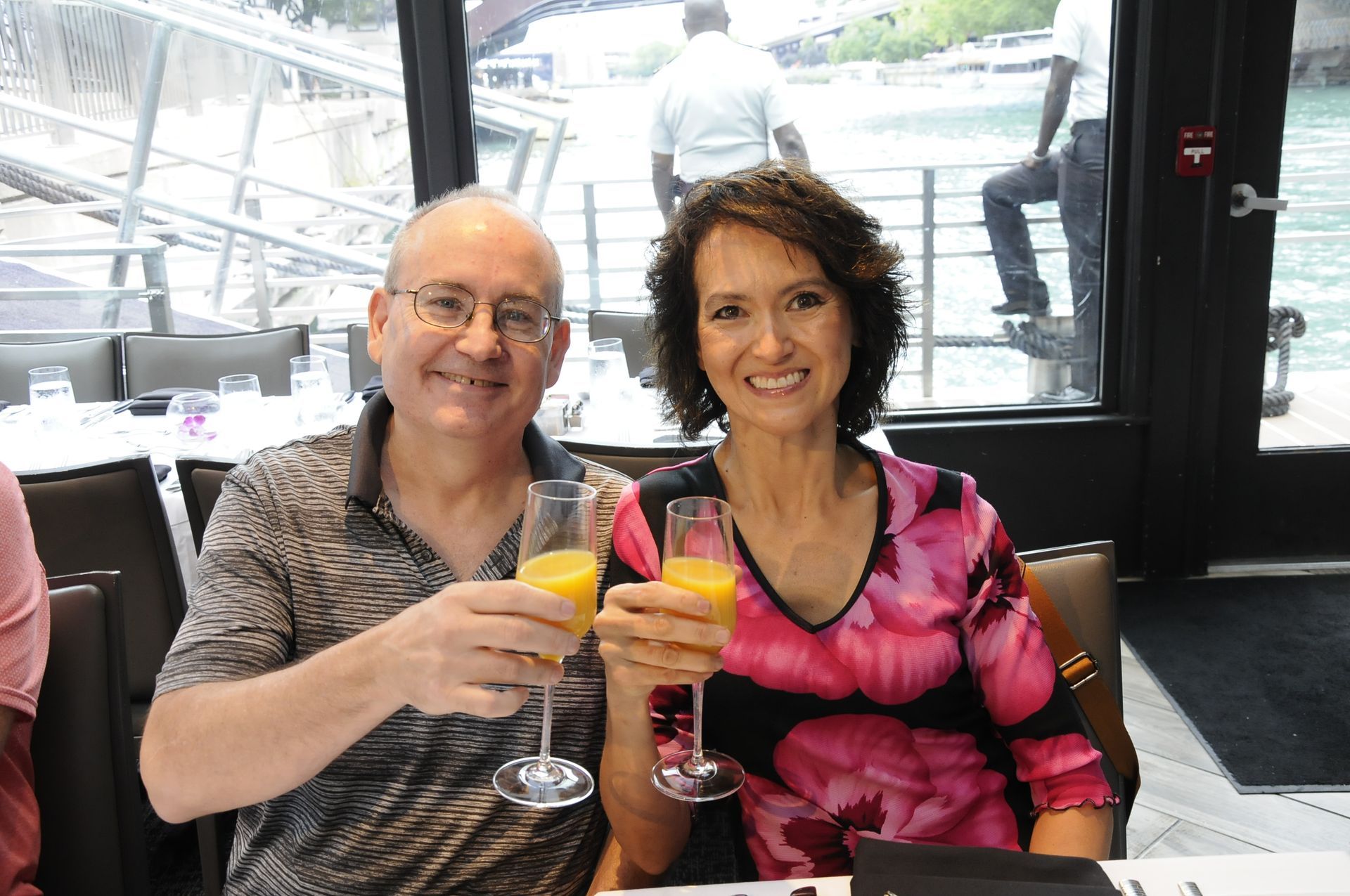 A man and a woman are sitting at a table holding glasses of orange juice.