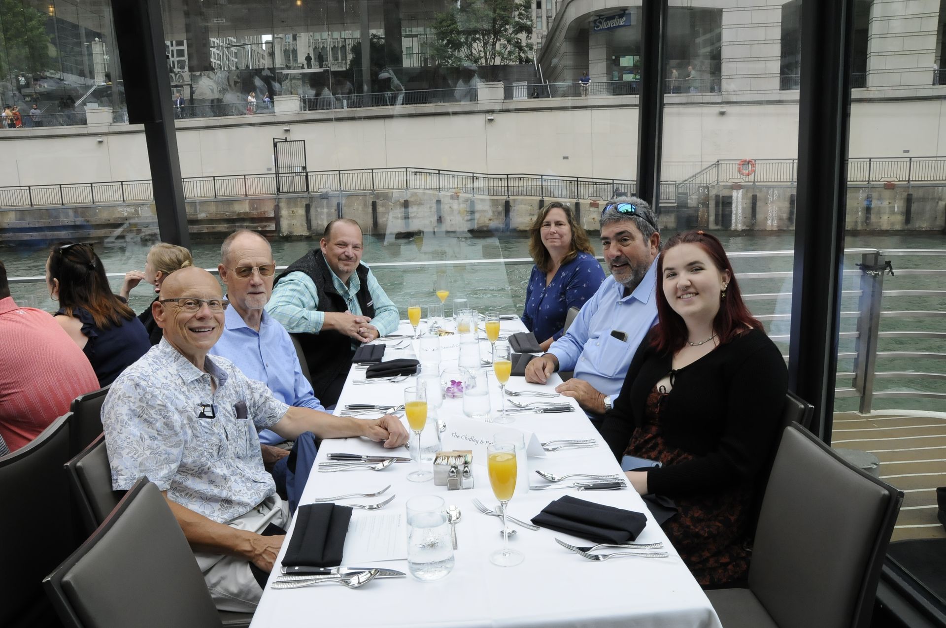 A group of people are sitting at a long table with glasses of wine.